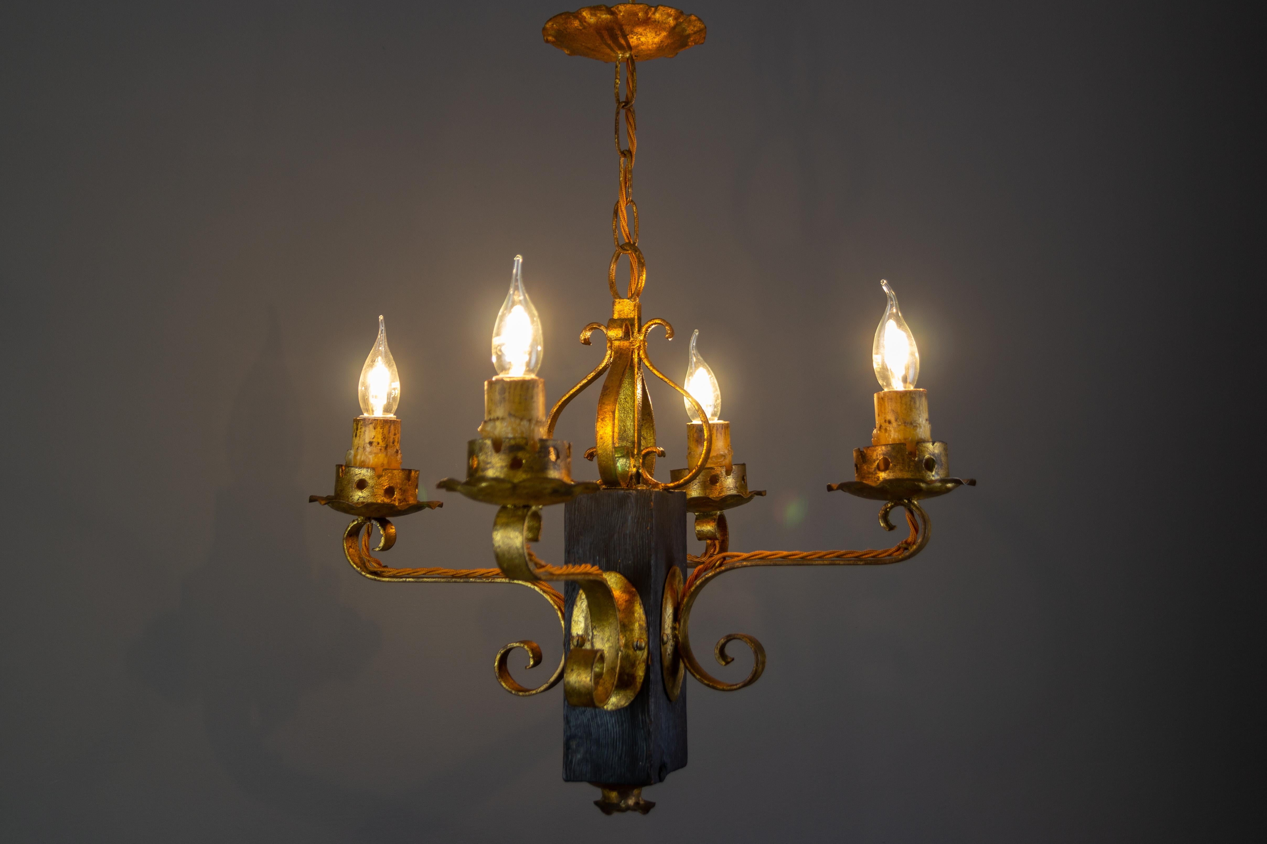 Gilt wrought iron and black wood four-light chandelier or pendant light, Spain, 1930s.
This beautifully crafted and one-of-a-kind light fixture features a black and rectangular wooden base with a golden wrought iron arm on each side.
It is a perfect