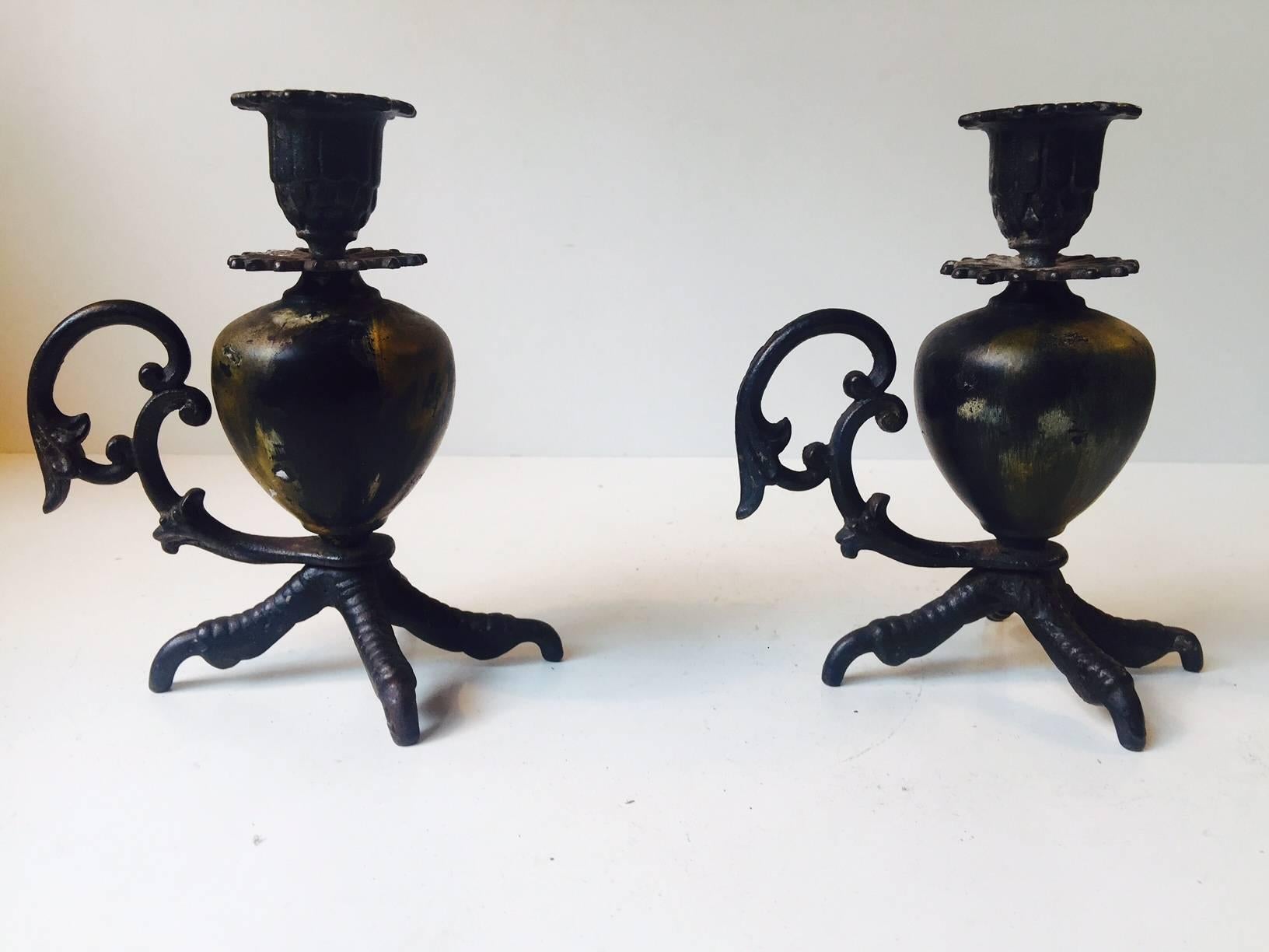 A pair of wrought iron candlesticks featuring talon claw bases, glazed ceramic baluster shaped centrepieces and detailed Gothic handles. They are of European origin, presumably France.