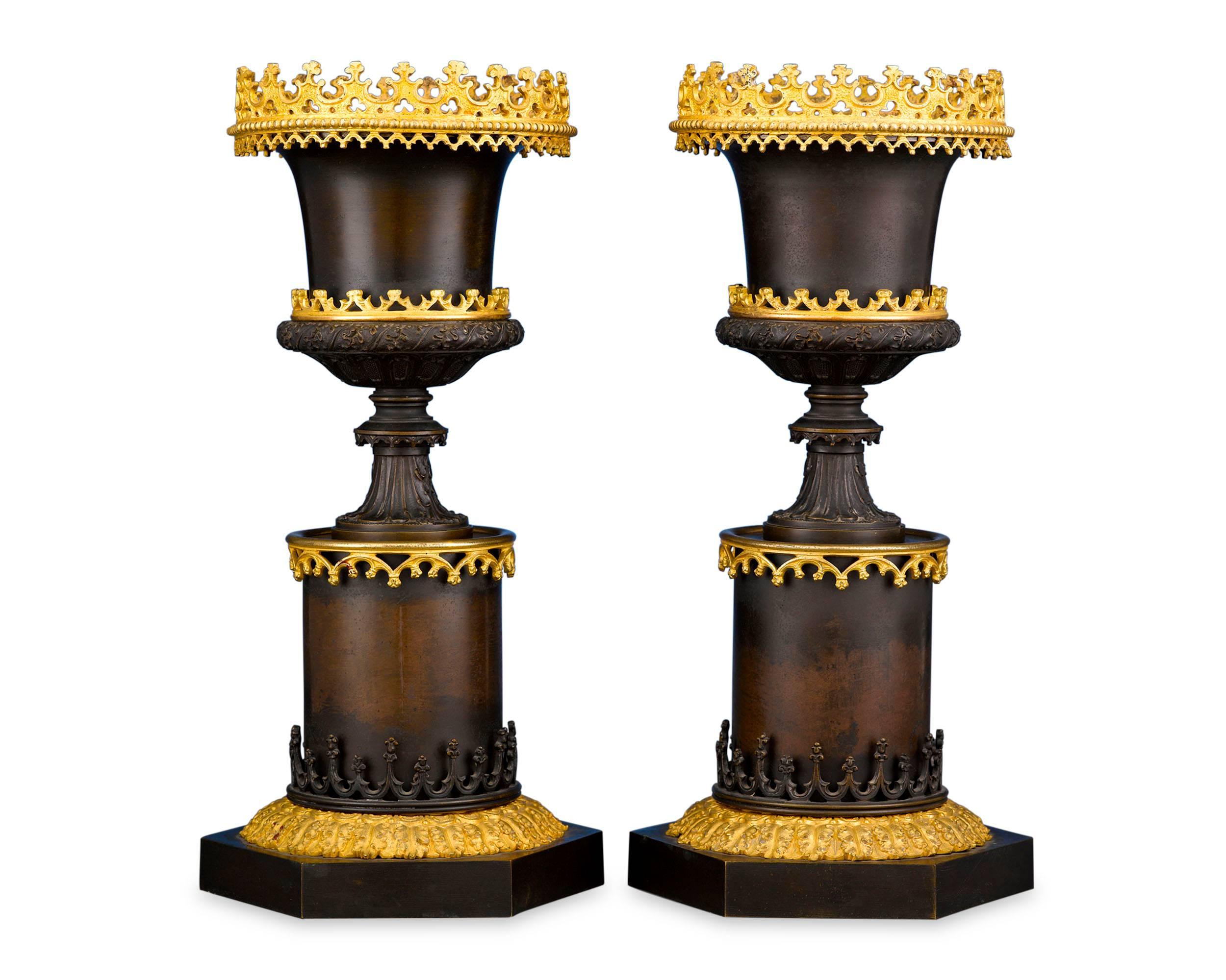 A striking pair of bronze urns, created in the dramatic Gothic style. Resembling classical Greco-Roman vases set upon pedestals, the urns are crafted in a two-toned design, with deep burnished bronze bodies and three galleries of ornate bronze