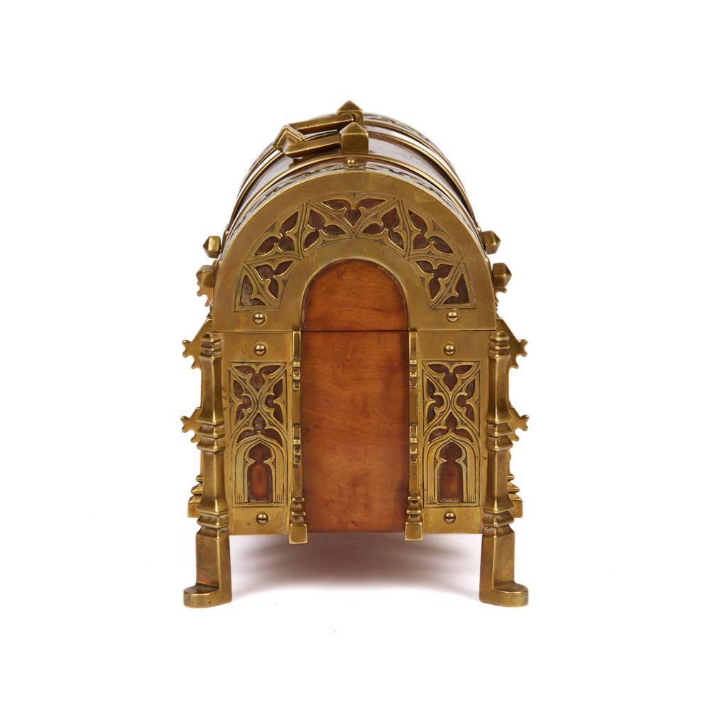 A stunning Arts & Crafts Gothic walnut and bronze jewellery casket of domed shape in the manner of A.W.N. Pugin. The casket stands raised on four corner legs with a domed hinged cover with an articulated handle and pierced strapwork decoration. The