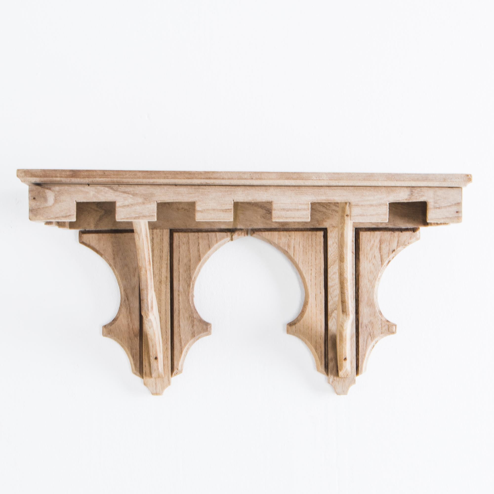 This wooden wall console from turn of the century Belgium has a striking Gothic design, featuring a decorative crenellated apron and peaked, buttress-style struts. Made of oak and recently restored to a light understated finish. This wall console is