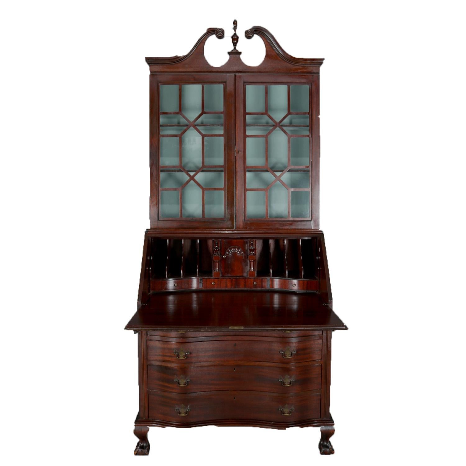 Governor Winthrop secretary features mahogany construction with broken arch pediment over two glass front doors opening to bookshelf with painted interior seated on slant drop front desk opening to reveal writing surface with storage drawers and
