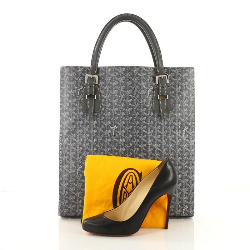 This Goyard Comores Tote Coated Canvas GM, crafted from gray coated canvas, features dual leather handles with buckle detailing, protective base studs, and silver-tone hardware. Its wide open top showcases a yellow fabric interior with side zip