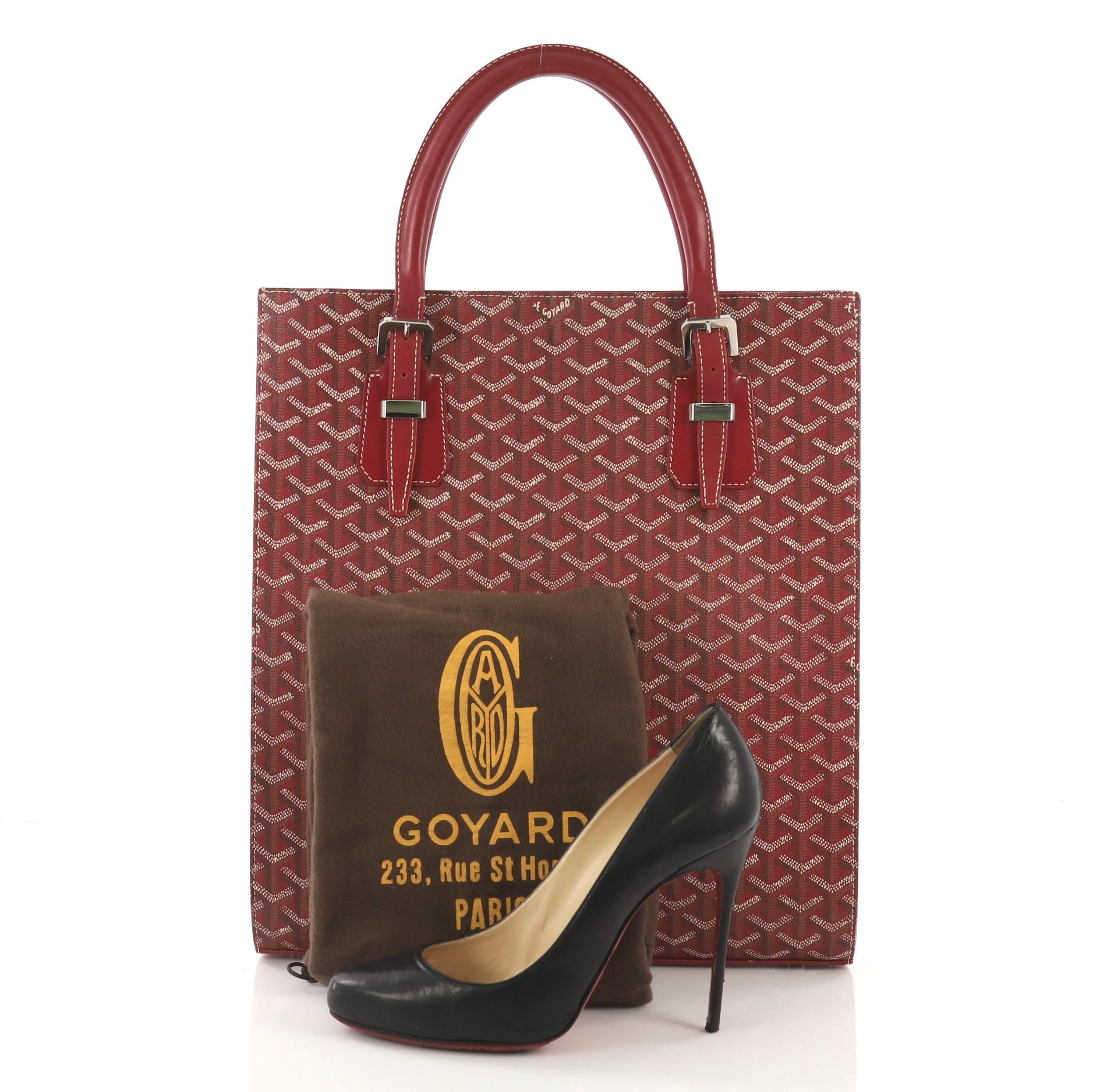 This Goyard Comores Tote Coated Canvas GM, crafted from red chevron coated canvas, features dual leather handles with buckle detailing, leather trim, protective base studs and silver-tone hardware. It opens to a yellow fabric interior with side zip