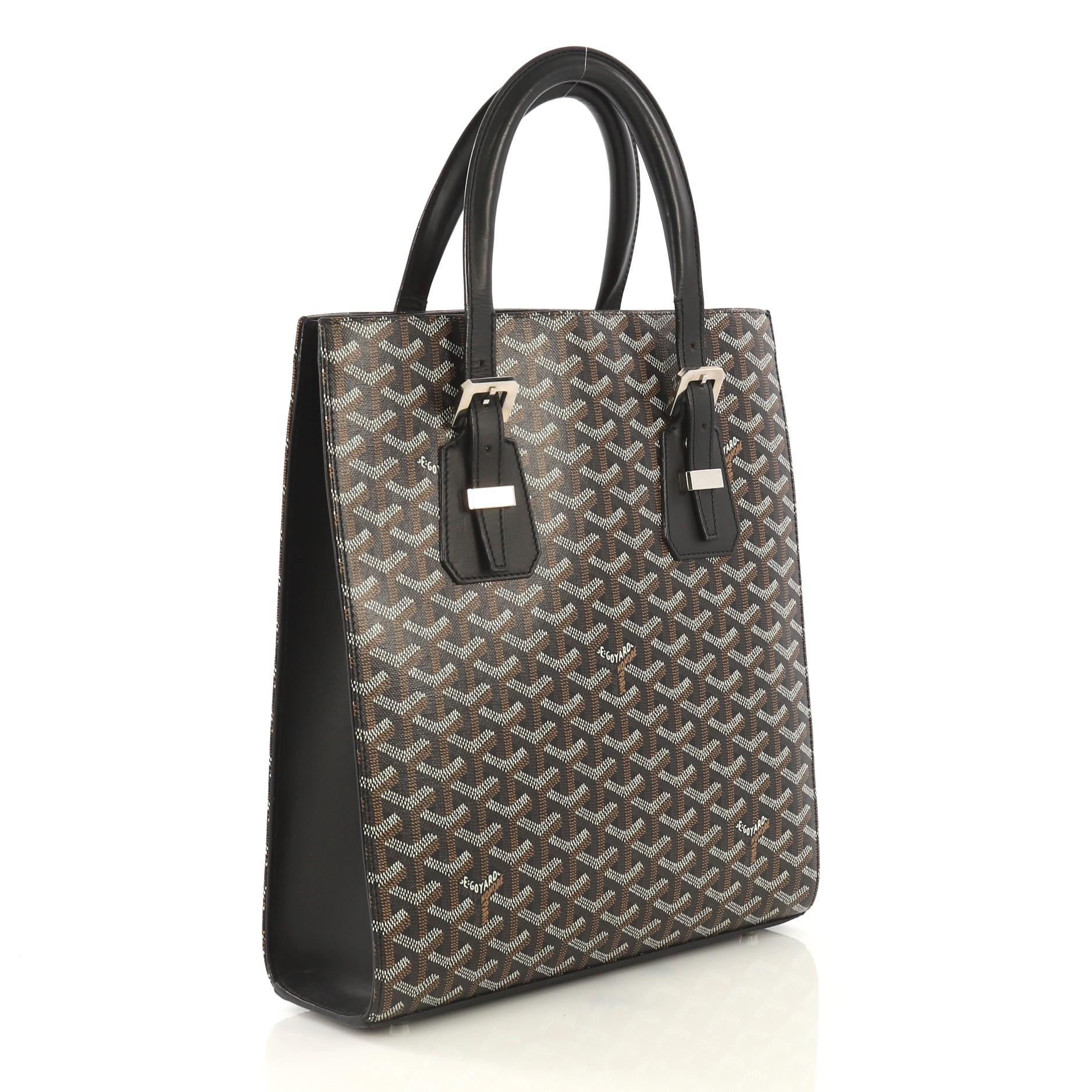 This Goyard Comores Tote Coated Canvas PM, crafted from black coated canvas and leather, features dual leather handles with buckle detailing, leather trim, and silver-tone hardware. It opens to a yellow fabric interior with side zip pocket.