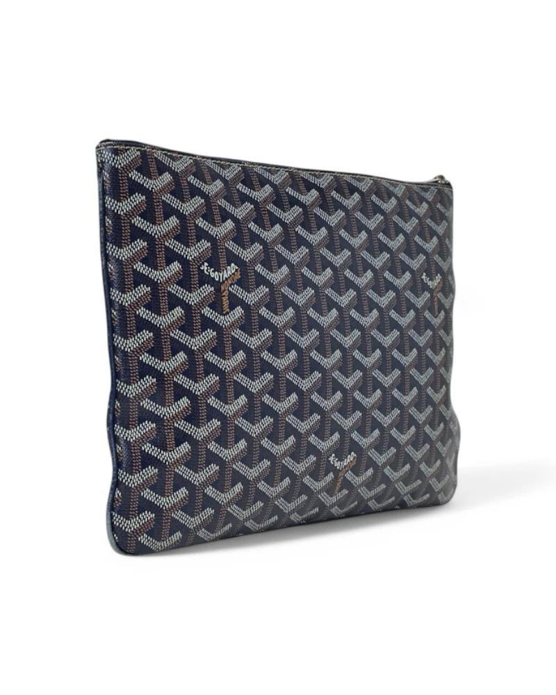 Pochette signée Goyard, modèle Senat en taille MM, en toile bleu marine avec garnitures en cuir et ferrures argentées. Dotée d'une fermeture à glissière sur le dessus et doublée intérieurement en toile jaune avec une petite poche, la pochette est