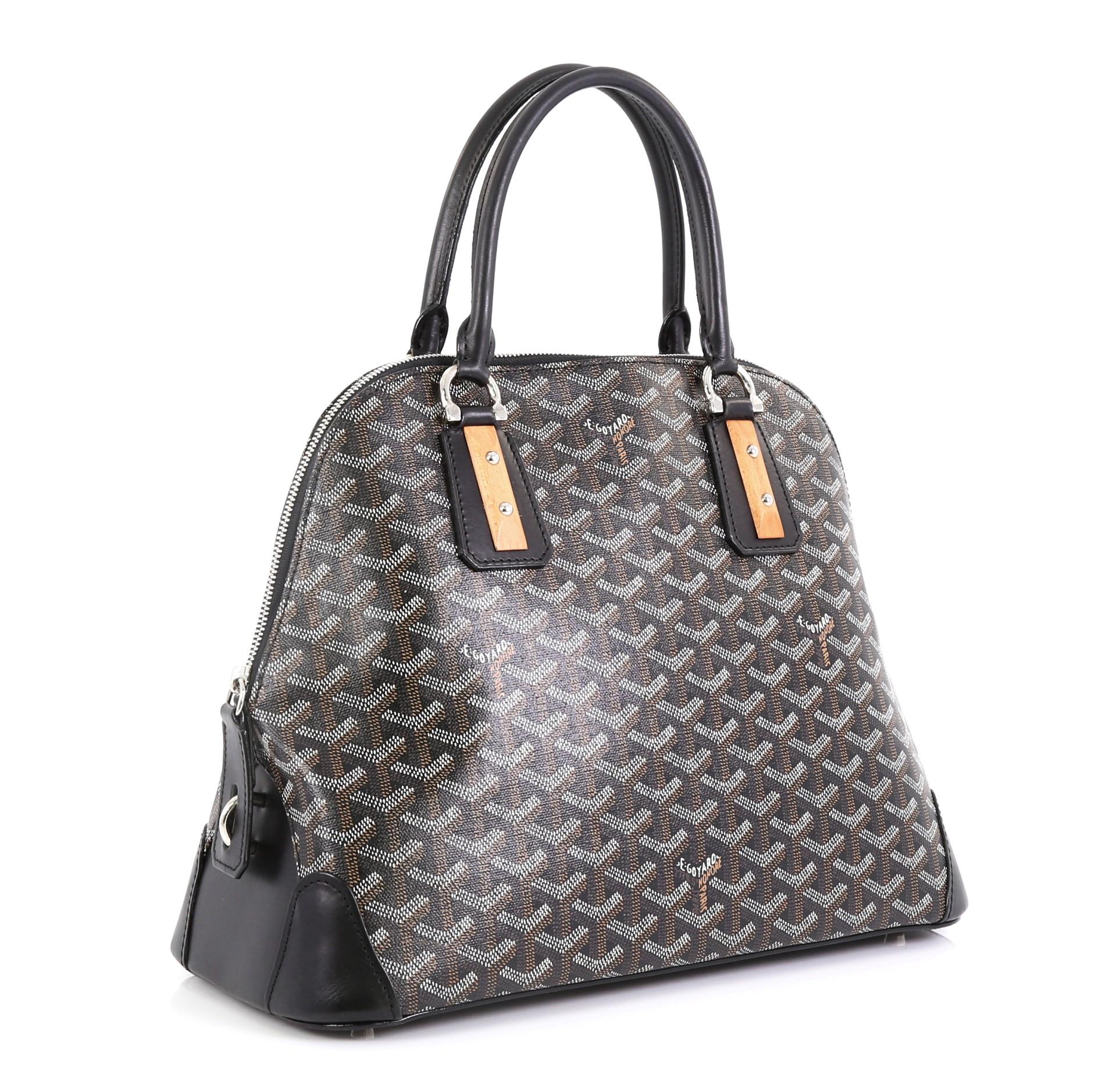 This Goyard Sac Vendome Handbag Coated Canvas PM, crafted from black and brown coated canvas, features dual rolled handles with wooden and stud details, leather trim, protective base studs, and silver-tone hardware. Its zip closure opens to a yellow
