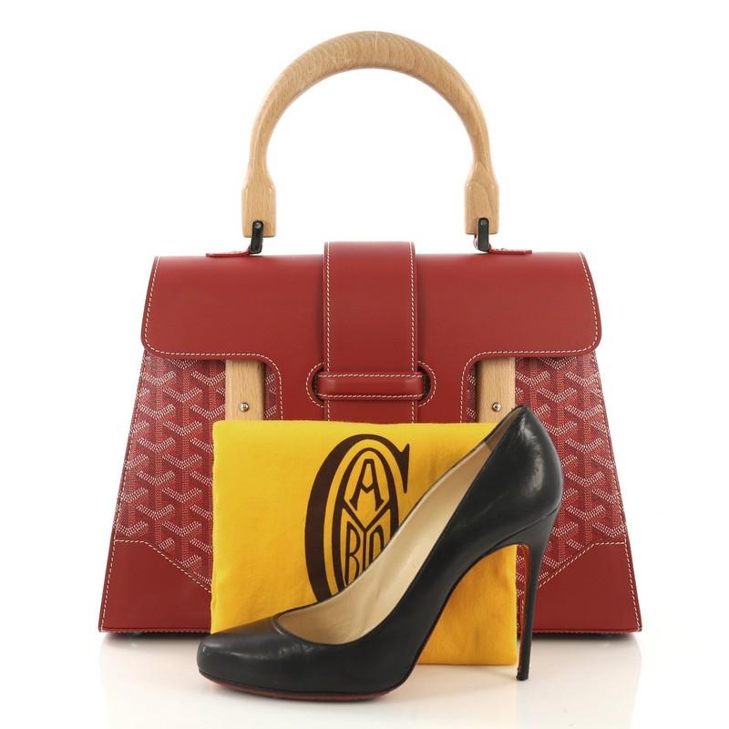This Goyard Saigon Top Handle Bag Coated Canvas with Leather MM, crafted in red coated canvas with leather, features a single looped wood handle, wood details, protective base studs, and silver-tone hardware. Its flap slide closure opens to a yellow