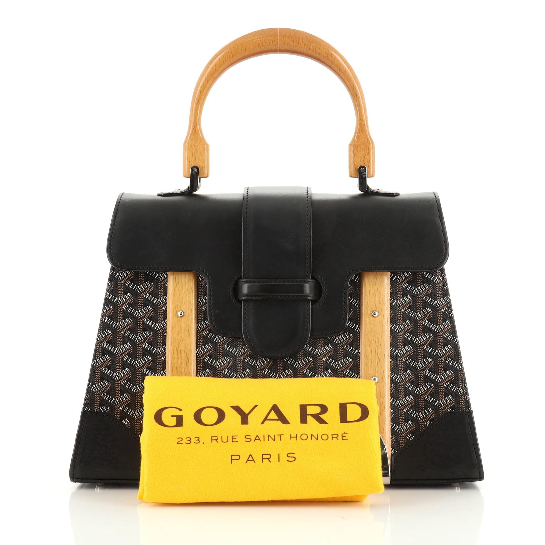 This Goyard Saigon Top Handle Bag Coated Canvas with Leather MM, crafted in black coated canvas with leather, features a single looped wood handle, wood details, protective base studs, and silver-tone hardware. Its flap slide closure opens to an