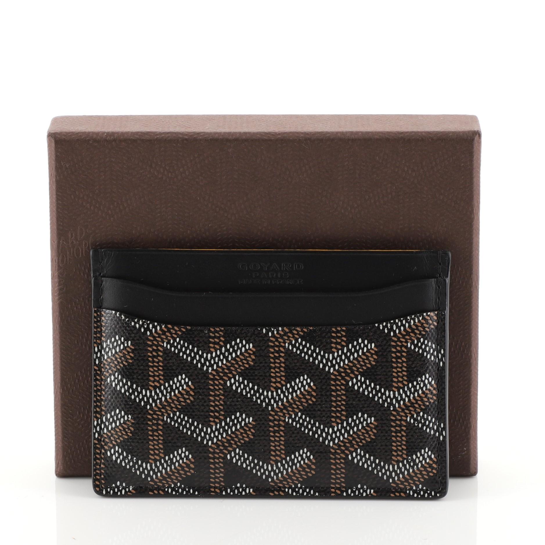 This Goyard Saint Sulpice Card Holder Coated Canvas, crafted from black coated canvas. It opens to a yellow leather interior with multiple card slots. 

Estimated Retail Price: $590
Condition: Great. Minor wear on base corners, faint scuffs on