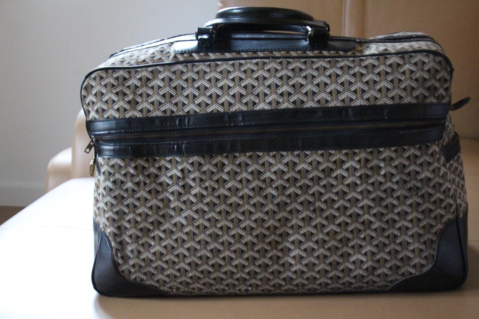 This beautiful Goyard bag features the very sought after combination of woven canvas and black leather. Its sturdy and comfortable handles are in black leather as well as its trims.
On its top, it opens thanks to its zip.It also has got a large zip