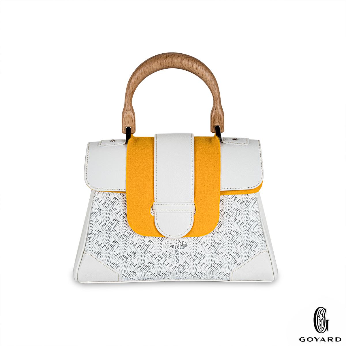 A sophisticated Mini Saigon handbag by Goyard. The exterior is crafted in the white signature Goyardine coated canvas with a wooden handle and foldover front lock that gives this bag a unique structure. The interior features a bright yellow calf