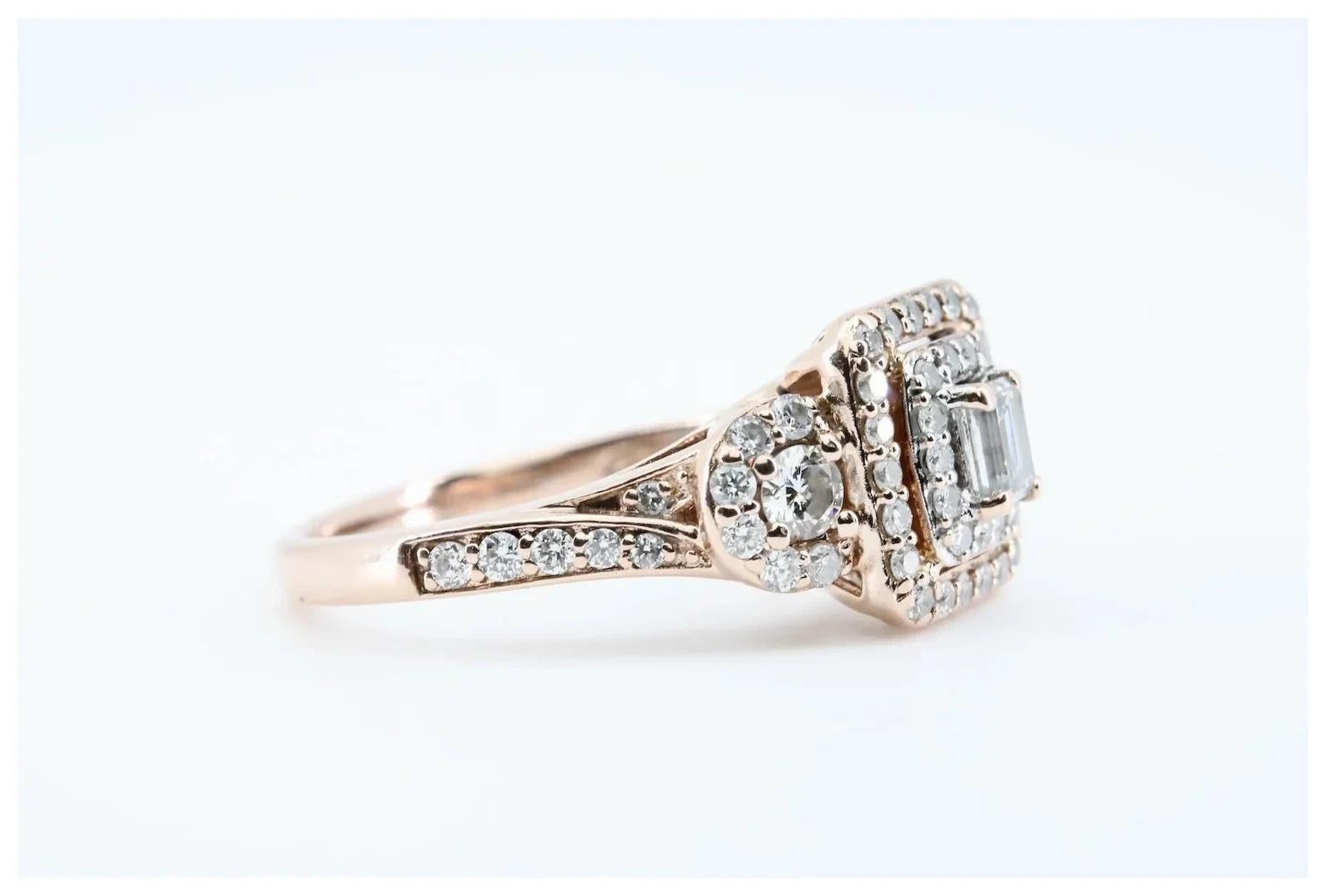 A delightful three stone diamond halo style ring crafted in 14 karat rose gold. Centering this ring is a 0.20 carat emerald cut diamond framed by a pair of 0.20ctw round brilliant cut diamonds. Encircling the three central diamonds are 62 pave set