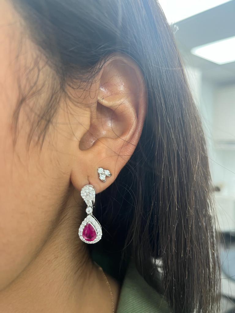 Embrace the enchanting beauty of these graceful 18 karat white gold earrings adorned with a delightful combination of rubies and diamonds. Each earring features a delicate pear-shaped ruby, totaling 2.06 carats, exuding a captivating red hue that