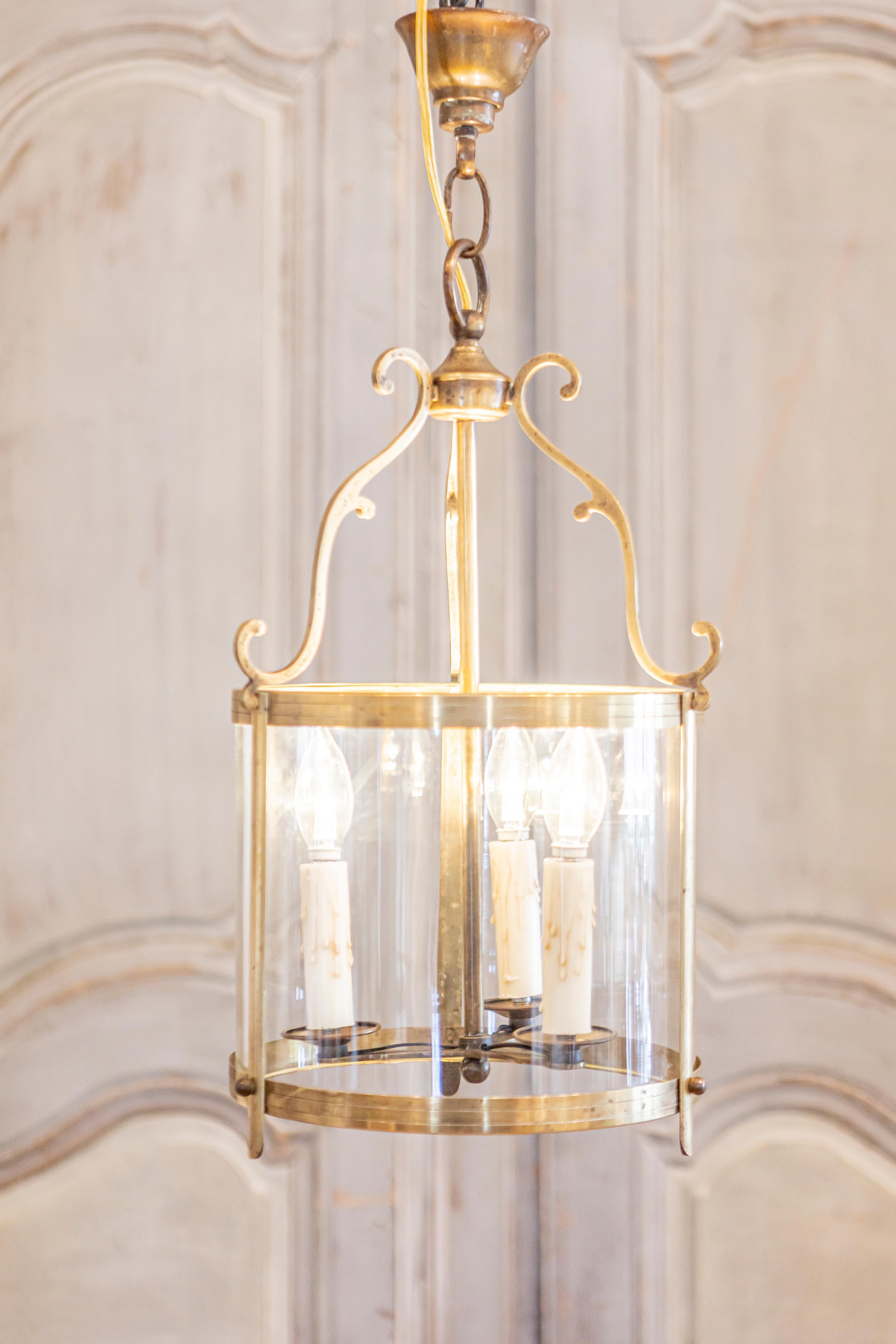 Este elegante farol francés de principios del siglo XX presenta un marco de latón bellamente elaborado con delicados soportes curvados, que le añaden un toque de refinamiento y encanto. El cuerpo cilíndrico está revestido de paneles de cristal