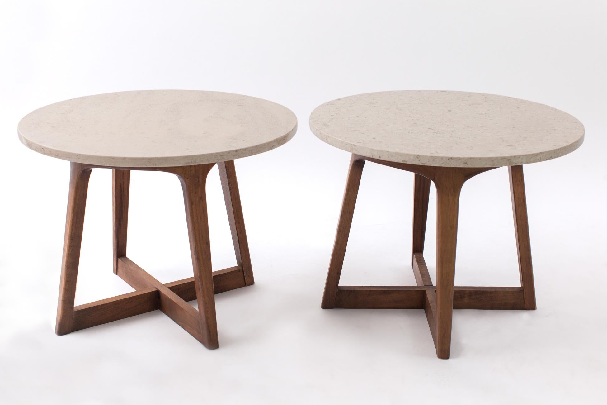 A graceful pair of sculptural end tables, with a circular cream-colored polished limestone top resting on an imbricate X-shape base in carved and tapering walnut, in the style of Adrian Pearsall. The round tops, incrusted with fossilized shells,
