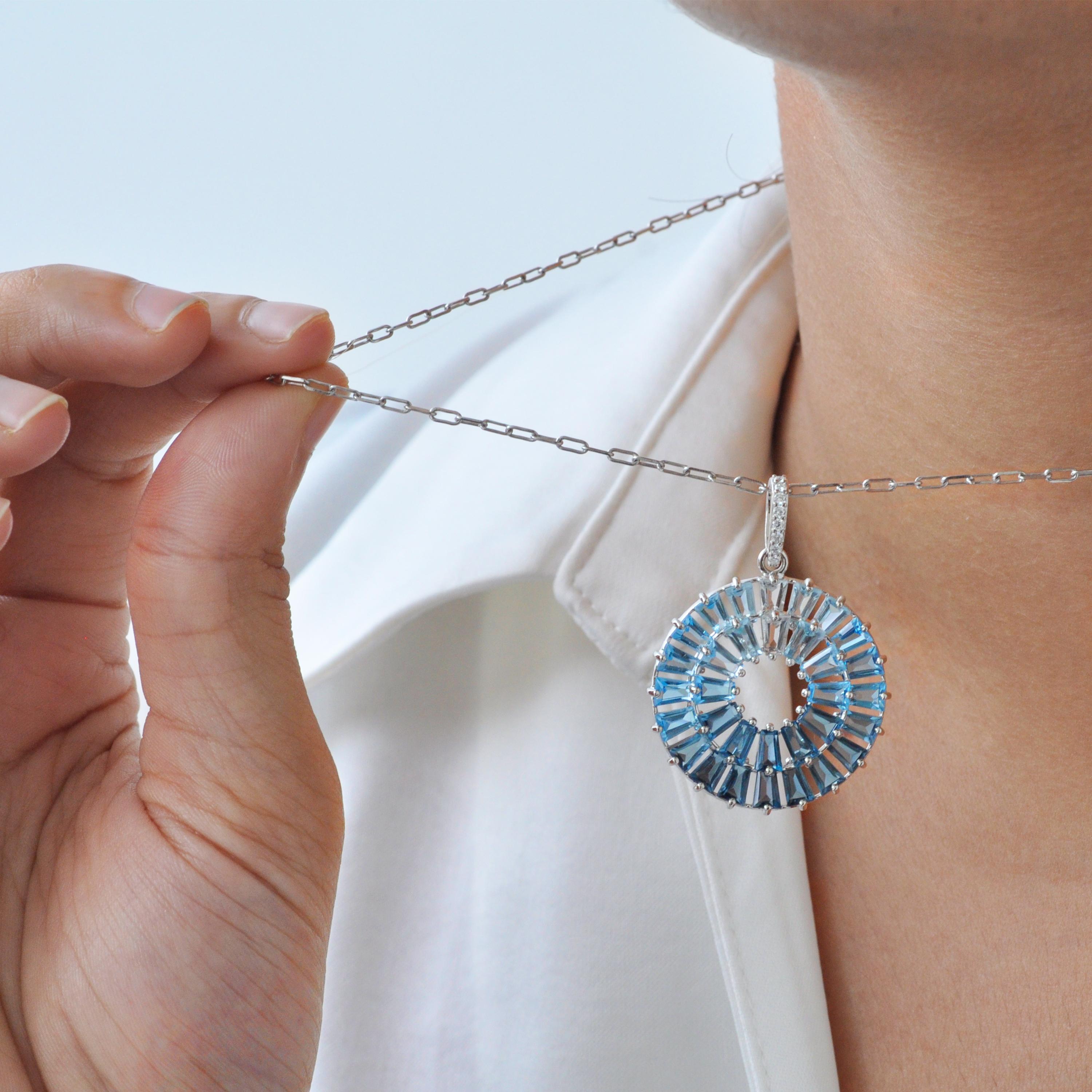 Questo elegante ciondolo, realizzato in oro bianco 14 carati, mostra un design circolare splendidamente strutturato che prende vita con una vibrante composizione di London Blue, Swiss Blue e Sky Blue Topaz. Ogni gemma è sapientemente modellata in
