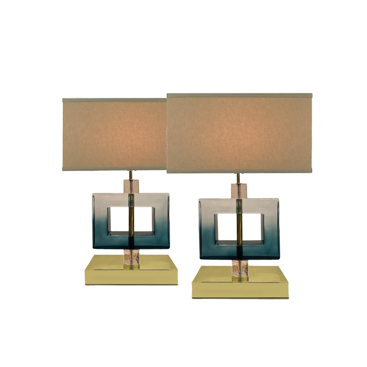 These elegant and sophisticated Murano glass table lamps have a sleek minimalist design based on geometric shapes. Two glass cubes cap a large glass square at the center to form the body of the lamps. Its dark teal glass color gradually becomes a