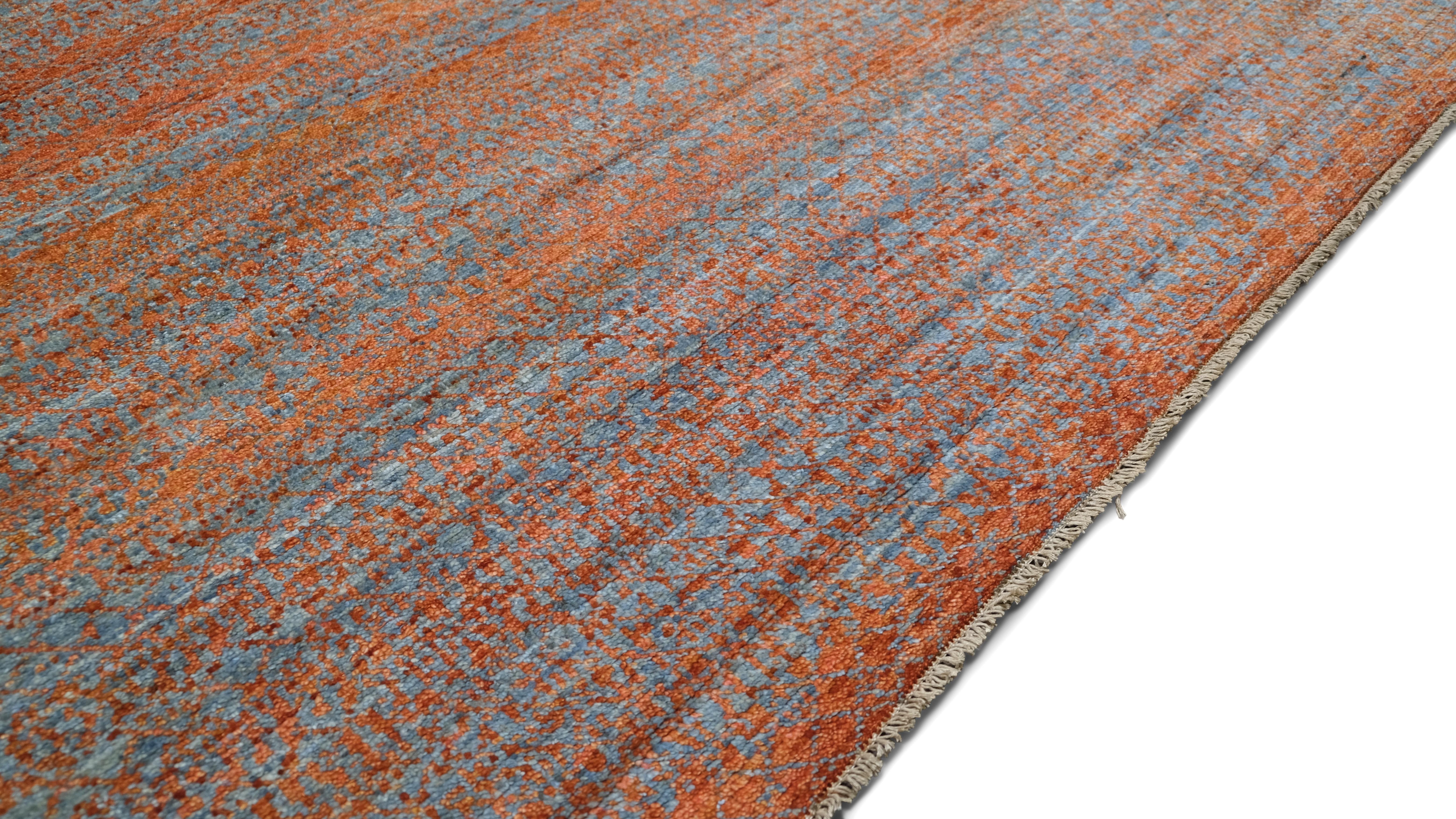 Dieser handgeknüpfte Wollteppich zeigt eine meisterhafte Mischung aus Tradition und moderner Kunst. Das weiche, strukturierte Design mit geschichteten Erdtönen in warmem Orange und gedämpften Blautönen verleiht dem Teppich eine ruhige und organische