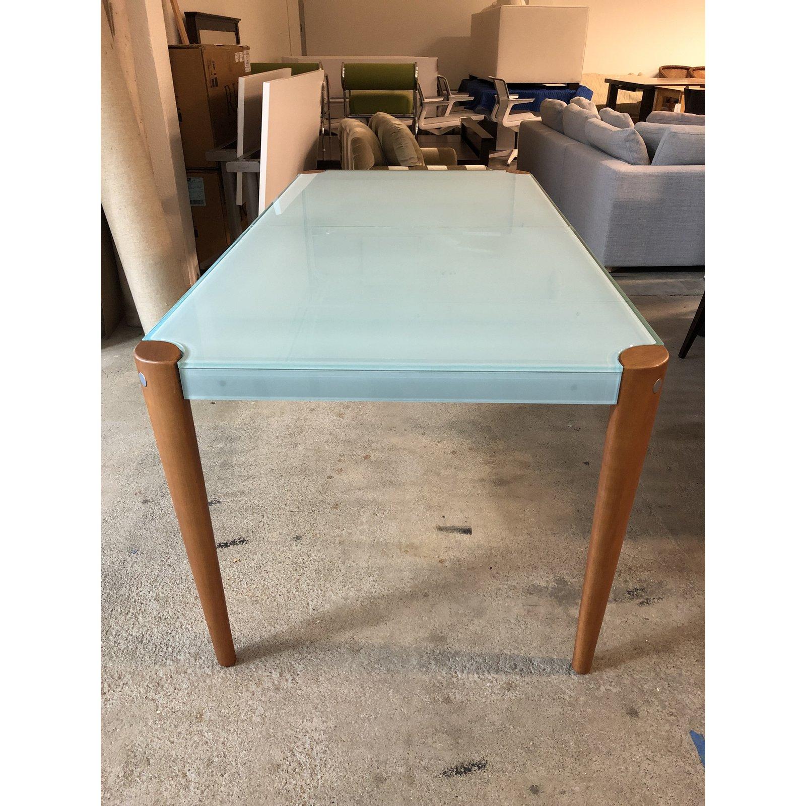 Design Plus Gallery presents an expandable table by Graebel. A frosted light seaglass table with four wood legs in a dark cherry finish. A butterfly leaf extension is hidden underneath the the glass. The table leaf is exposed by pulling one side of