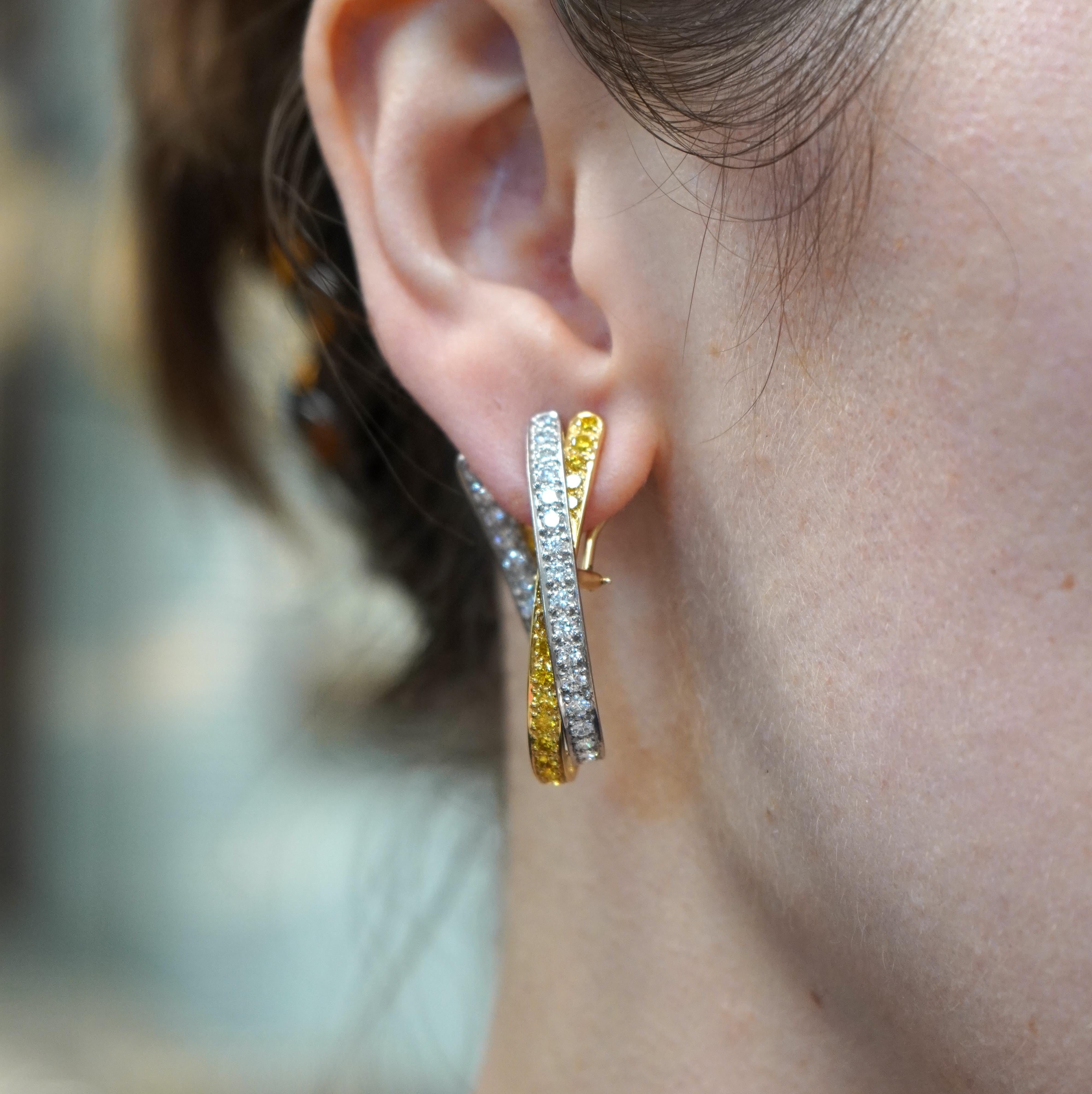 These Graff earrings from the 1990s are an elegant pair of open hoop crossover earrings, crafted in 14k white and yellow gold. Each earring features a stunning blend of white and fancy intense yellow diamonds, arranged in a round brilliant cut to