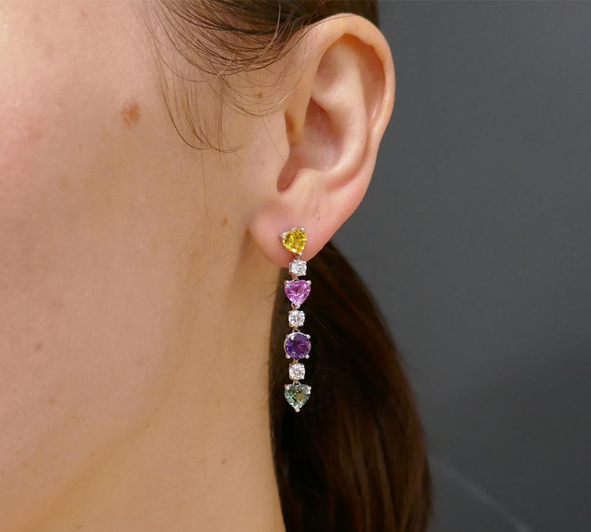 An elegant pair of Graff earrings, made of platinum, featuring diamonds and multi-colored sapphires. 
Each earring has three heart-shaped sapphires (yellow, pink, and green), one round sapphire (purple), and three round diamonds. The gems are set in