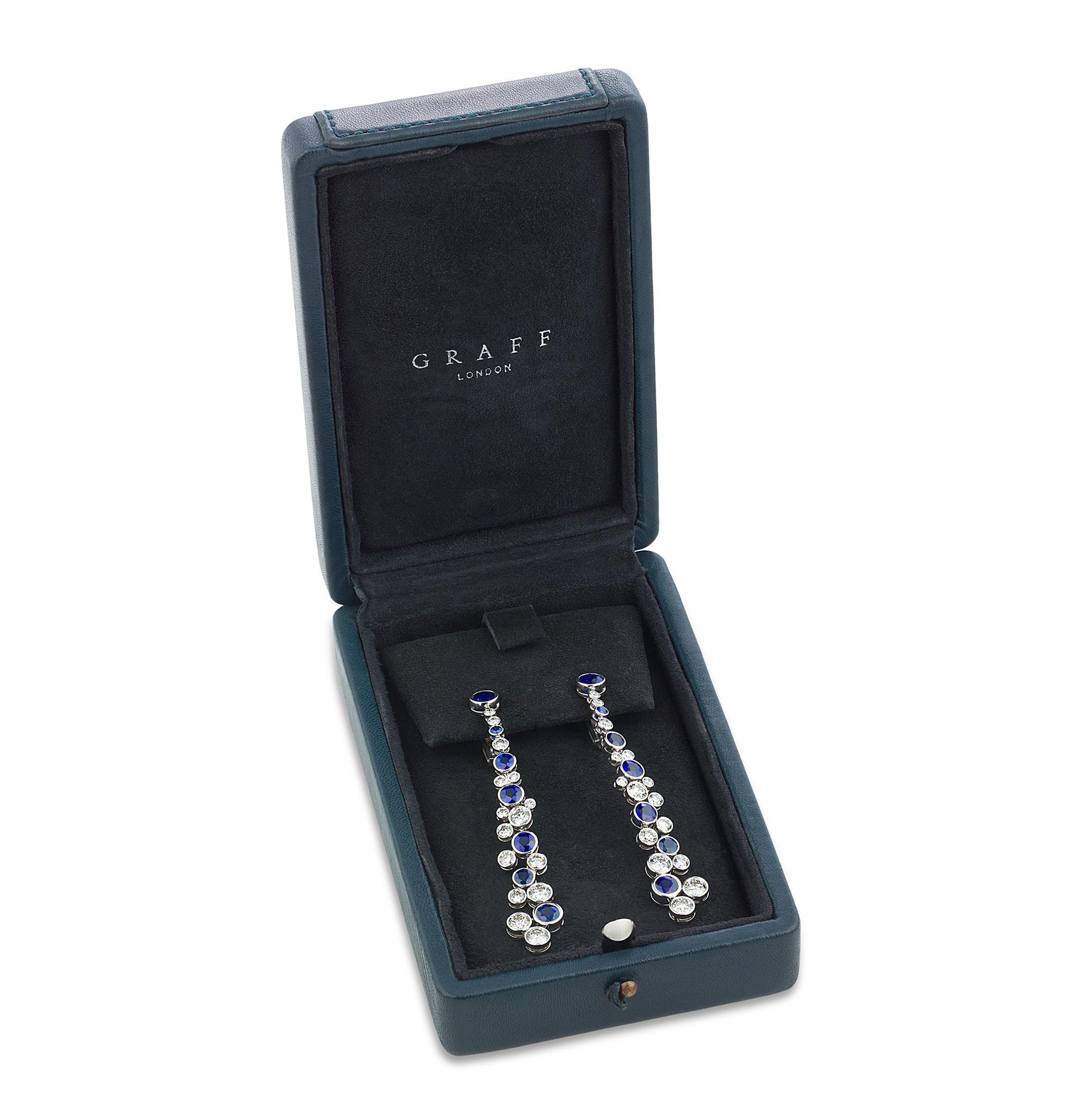 These exquisite drop earrings by the renowned jeweler Graff showcase round cut sapphires with a total weight of 6.23 carats and round brilliant cut diamonds totaling 3.98 carats. Set in 18K white gold, their elegant design cascades in a glimmer of