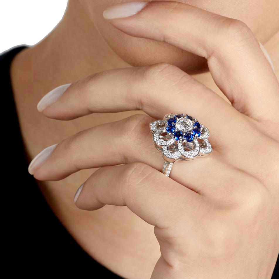 A magnificent Graff diamond cocktail ring showcasing a brilliant-cut diamond and sapphire frame openwork floral frame. The ring has round brilliant cut diamonds running down both sides of the band mounted in platinum. Signed Graff, with a ring size