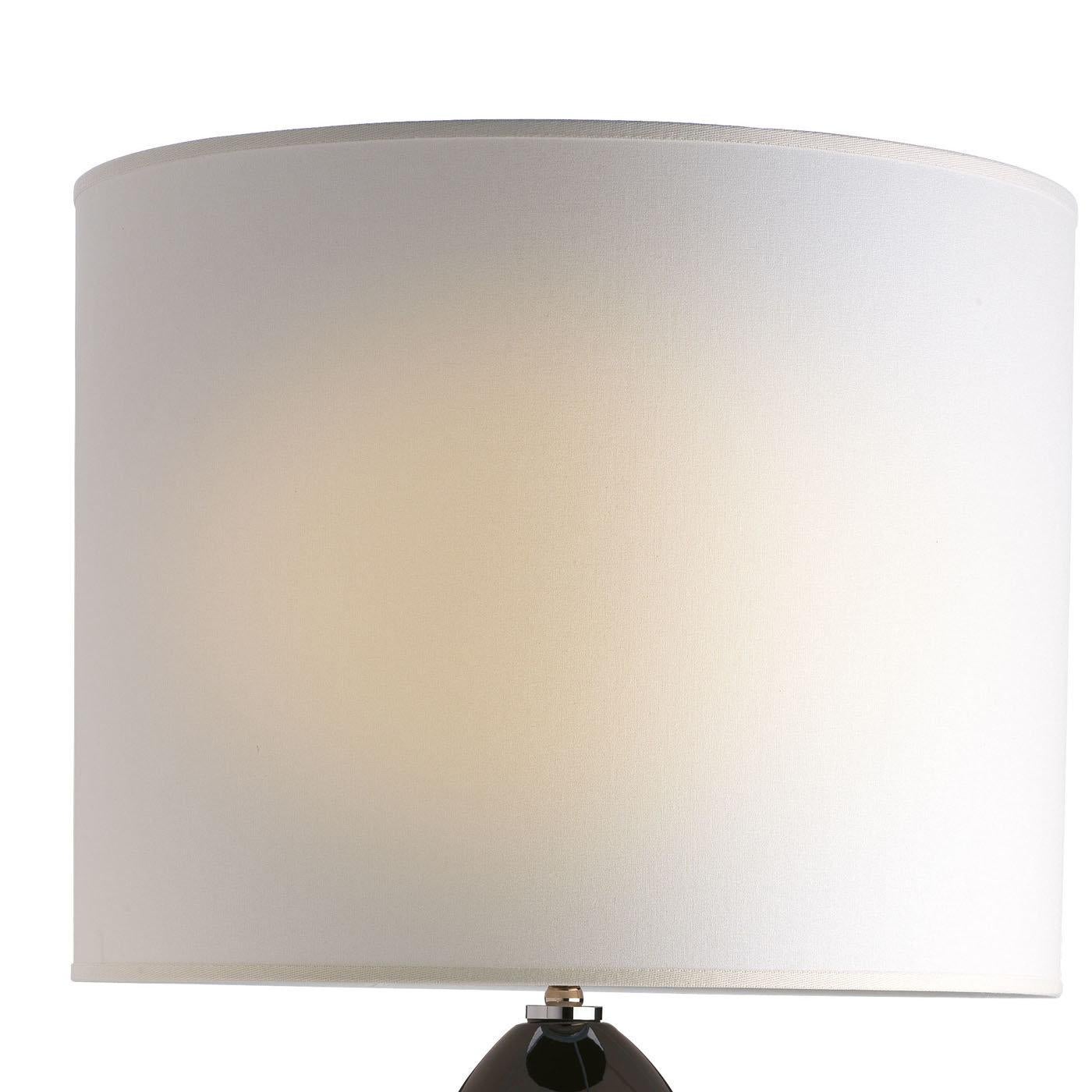 In this striking lamp, the brass shaft, featuring a glossy nickel finish, rests on top of a round brass base with the same finish and is encapsulated into a ceramic decoration made of four round elements painted a deep brown. The conic shade above