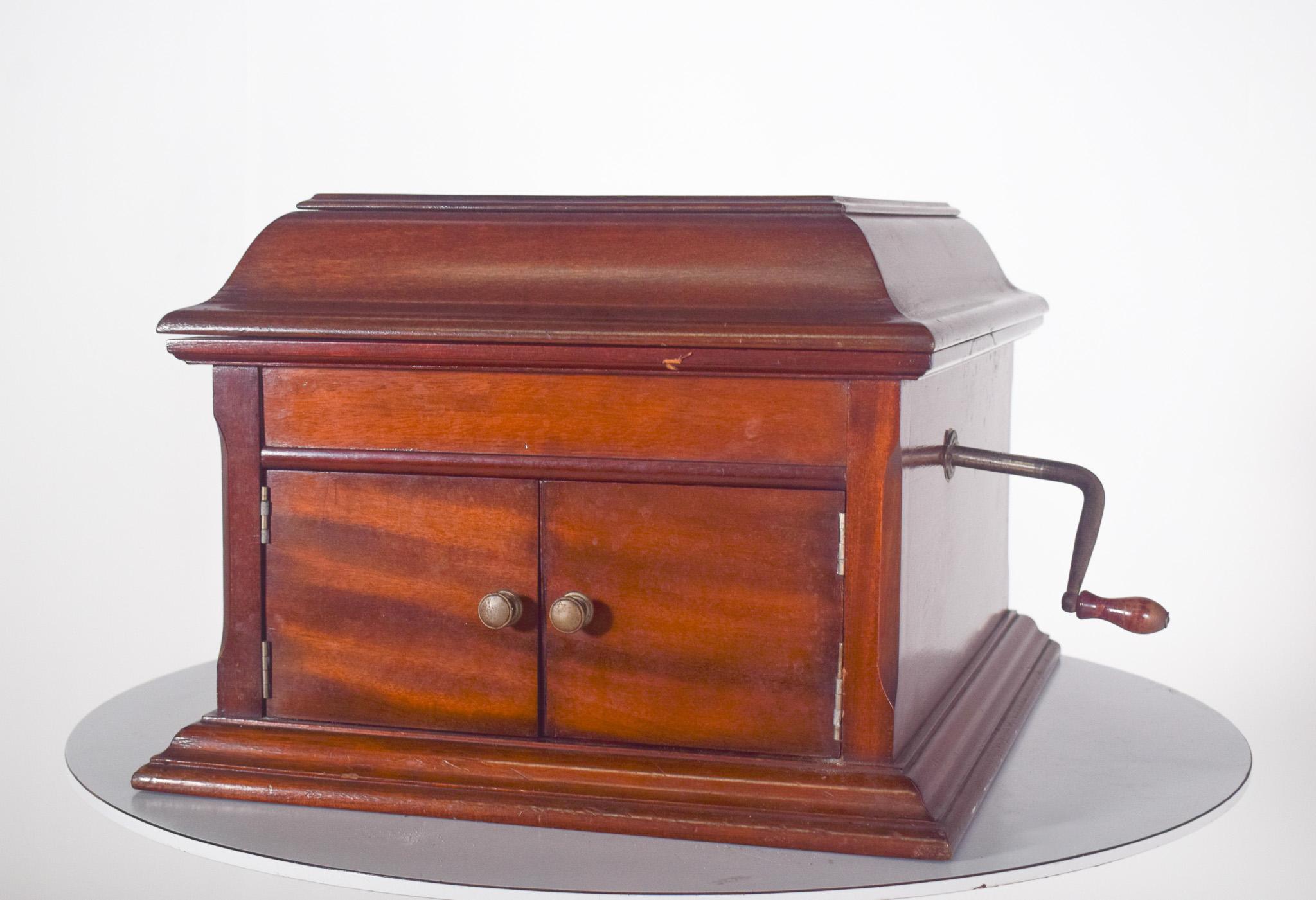 Grafonola, la Dulceola, avec coffret en bois. D'un design classique et élégant, l'appareil est fabriqué en bois verni, avec une finition raffinée et des détails bien travaillés. Le couvercle est ouvert, révélant la plaque recouverte de feutre vert