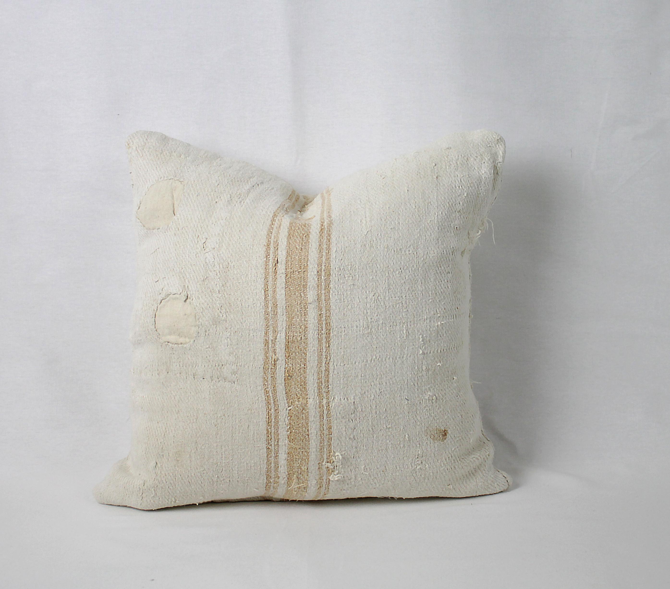 We make these pillows from old grain sacks from Eastern Europe. The pillow has a light orange triple stripe down the center, and the body is a medium oatmeal color. They are sewn with a zipper closure, and since we prewash all our vintage fabrics in