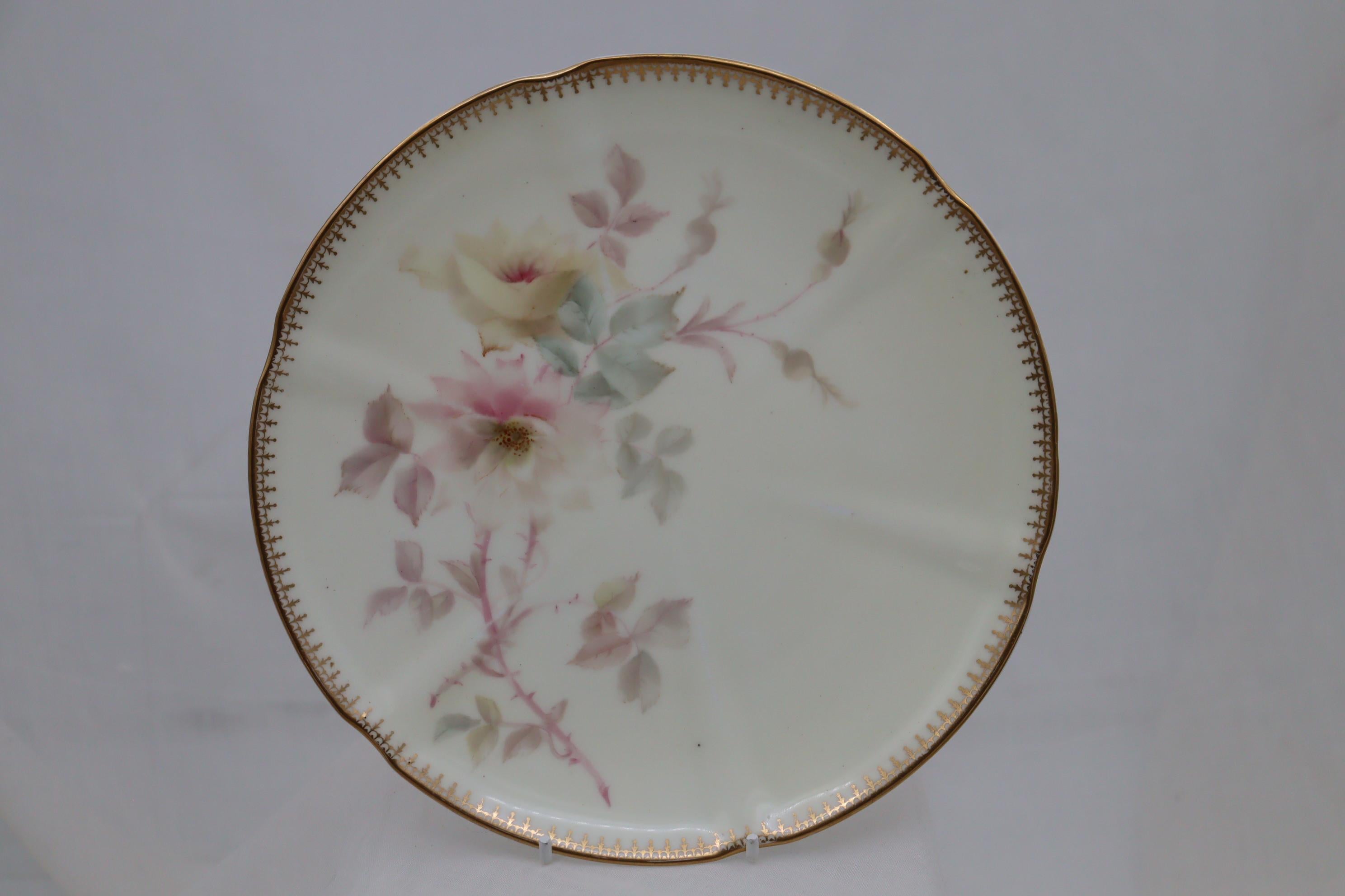 This hand painted and gilded porcelain part dessert service comprises two low comports and six plates and was made by the firm of Grainger's of Worcester. The very pretty painting of roses in delicate pastel colours on a pale cream ground is