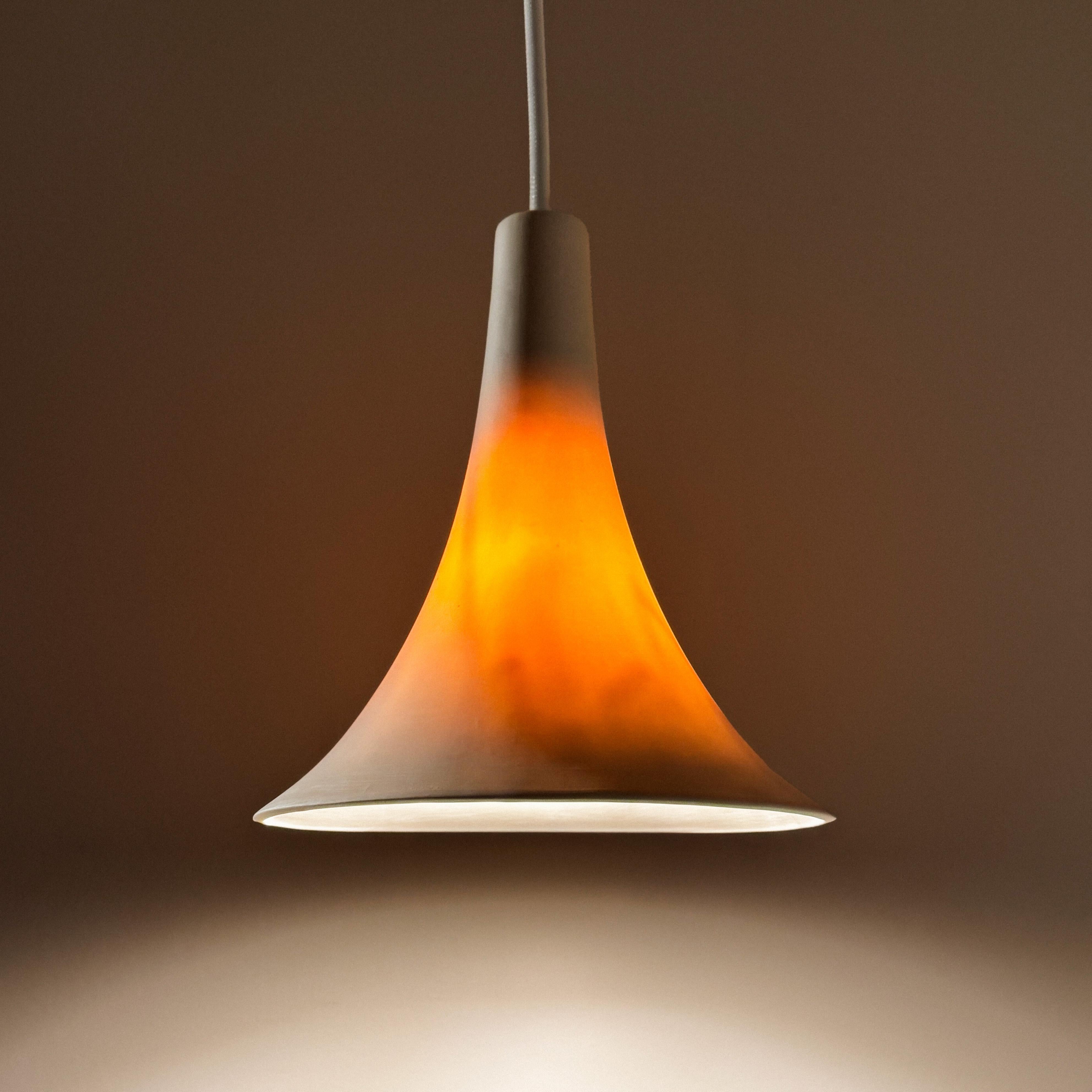 This gramophone shaped porcelain pendant lamp exudes understated elegance. When the light is off, the porcelain is matte warm white, and when the light is on, the pendant lamp glows with an amber hue, creating a calming ambiance. In addition to the