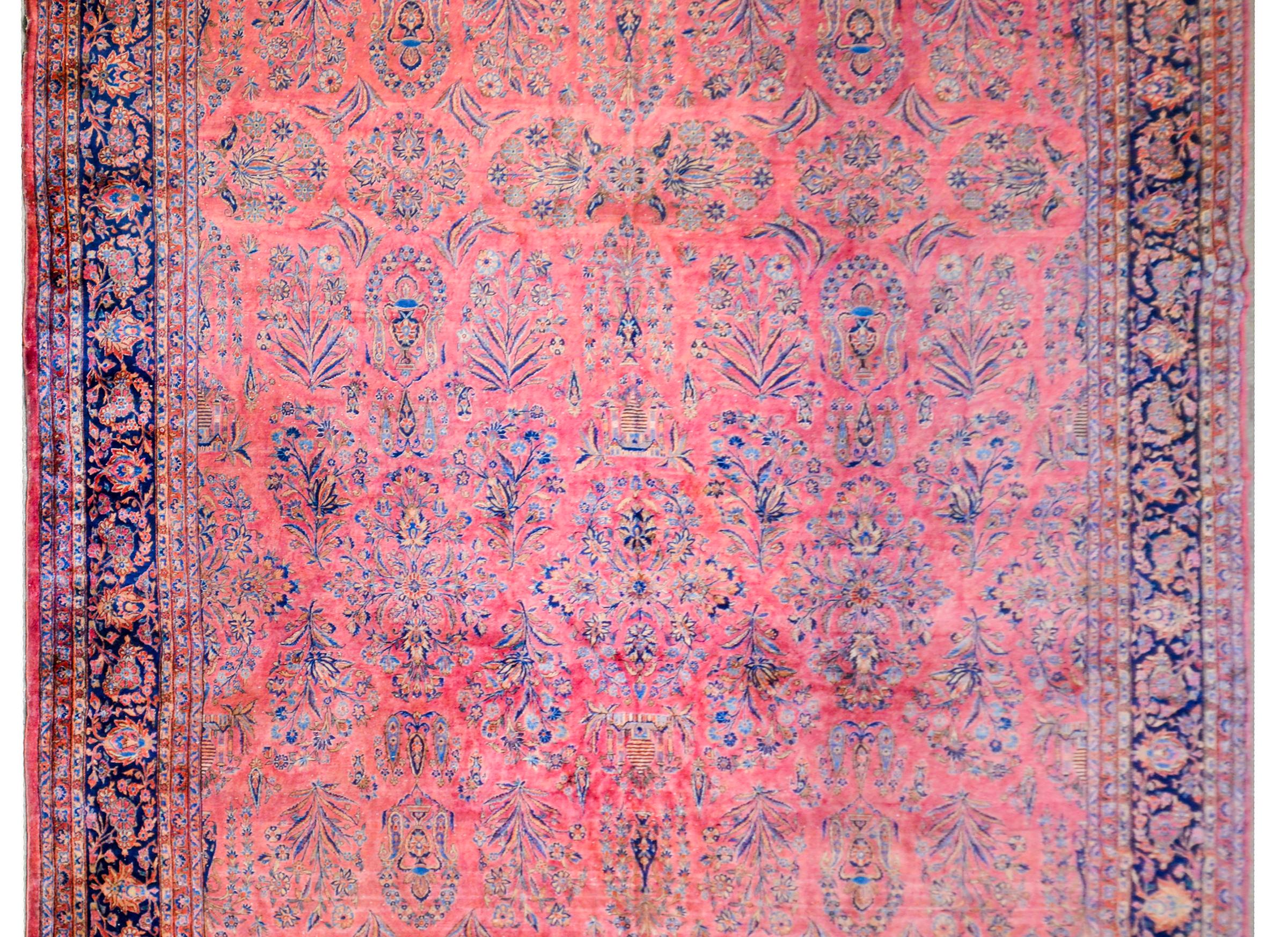 A grand 1920s Persian Kashan rug with a fantastic finely rendered pattern containing myriad flowers woven in light and dark indigo, beige, and gold, on a brilliant cranberry colored background. The border is complex with multiple pairs of petite