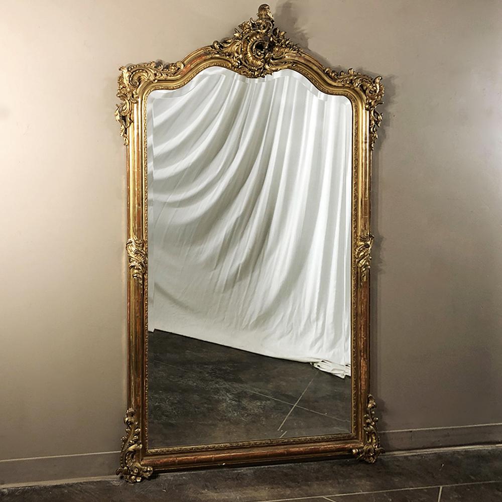 Measuring a full six feet tall, this elegant grand 19th century French Louis XV gilded mirror features its original gilding and silvering on the mirror, and boasts intricate detail from the Rococo Cartouche atop the arched crown all the way down to