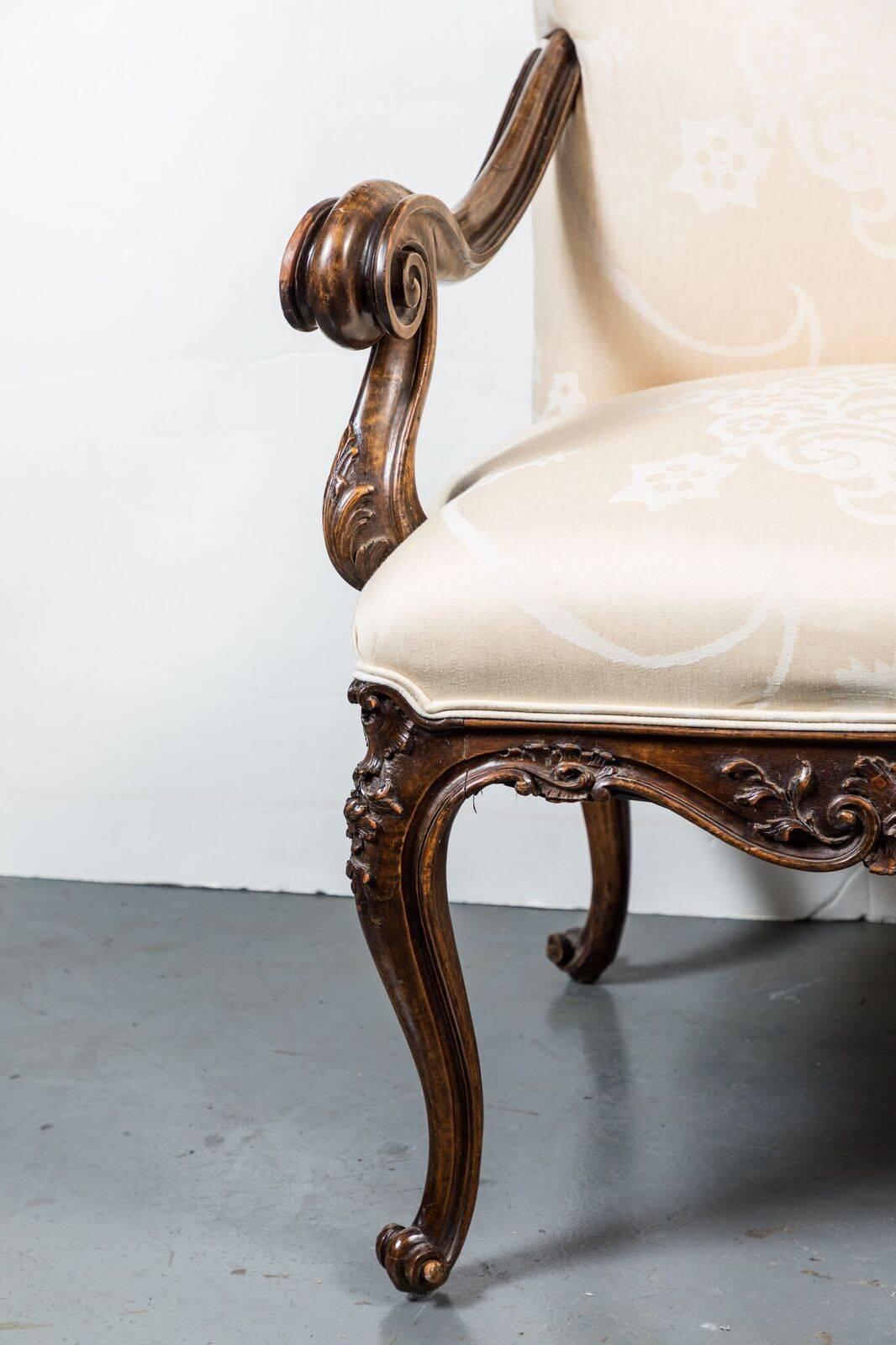Pair of large, Italian, walnut hall chairs featuring dramatic scrolling arms above a relief carved apron with foliate details. Each chair atop delicate scrolled feet. Upholstered in a luxurious, neutral, Nancy Corzine fabric.