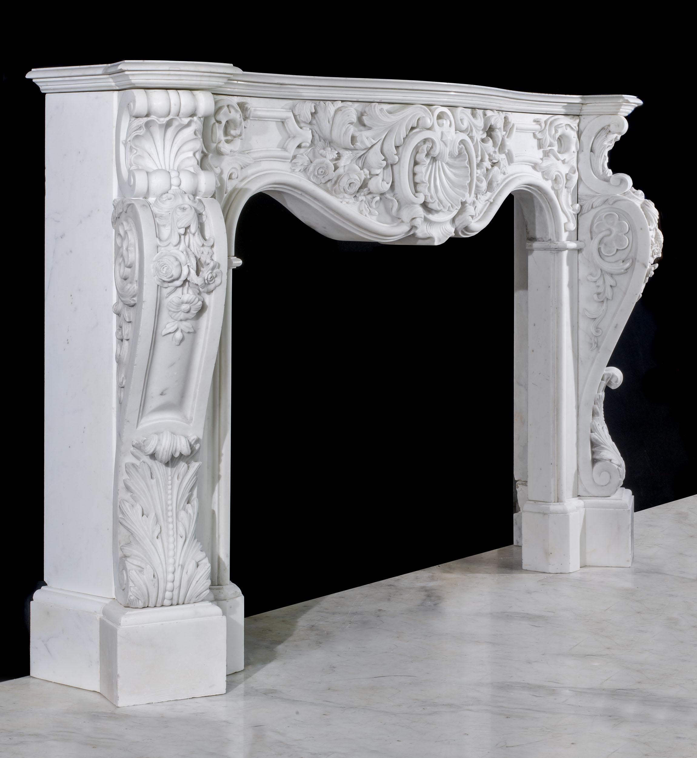 Un grande camino rococò in marmo bianco statuario, riccamente scolpito in alto rilievo per creare un vero e proprio pezzo forte. Il ripiano sagomato a serpentina ospita un fregio ornato, intagliato con foglie e fiori d'acanto stilizzati, centrato da