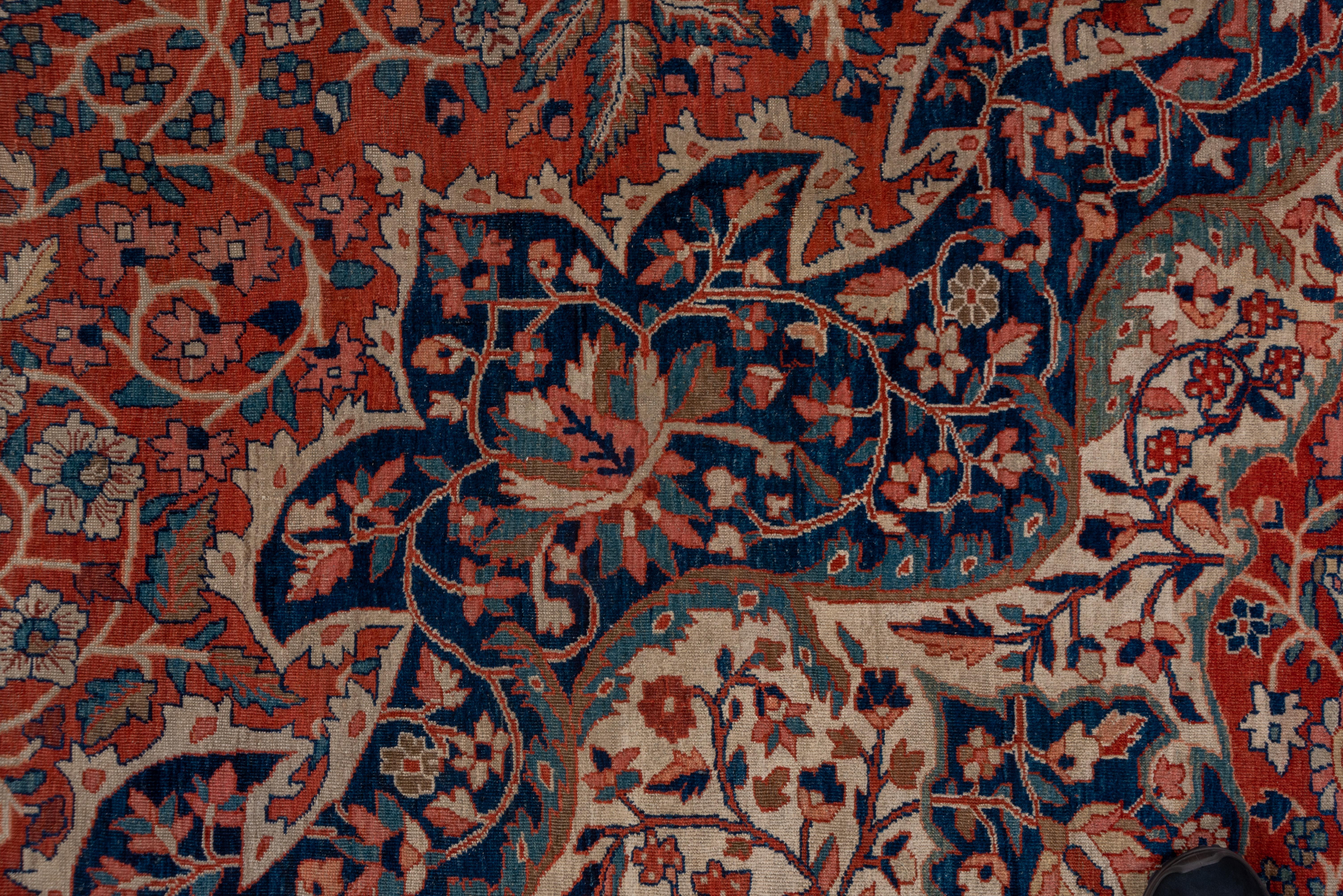 An elaborately octofoiled navy medallion with a sand bumpy lozenge sub-medallion with en suite extended corners, is set on the rust-red field with a dense floral arabesque pattern. Narrowi navy border of pointed oval palmettes with connecting fat
