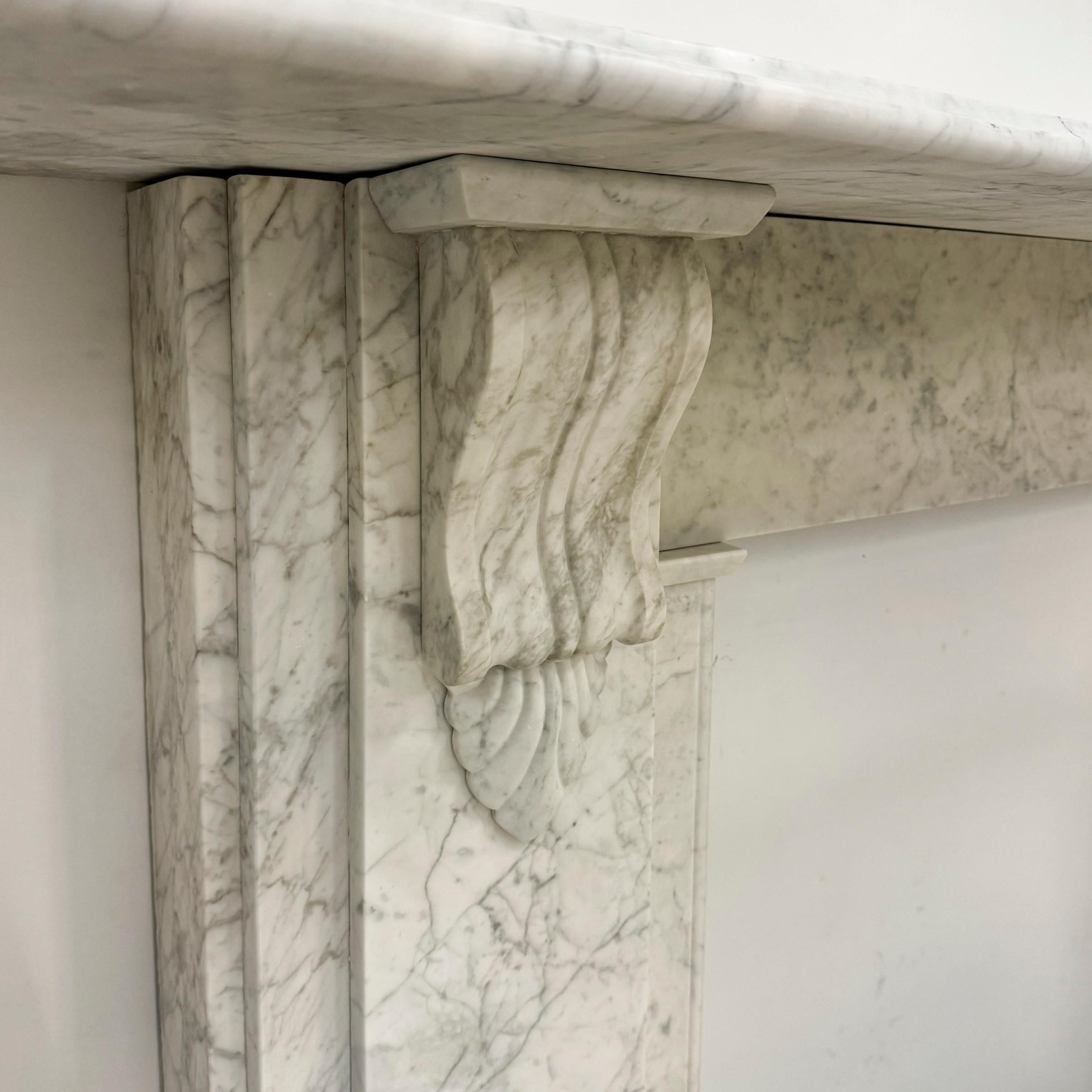 Un grande camino vittoriano in marmo di Carrara. 

Questo camino a mensola in marmo di Carrara di epoca previttoriana presenta un ripiano elegantemente modellato e sostenuto da mensole intricatamente intagliate. Il design mette in evidenza il