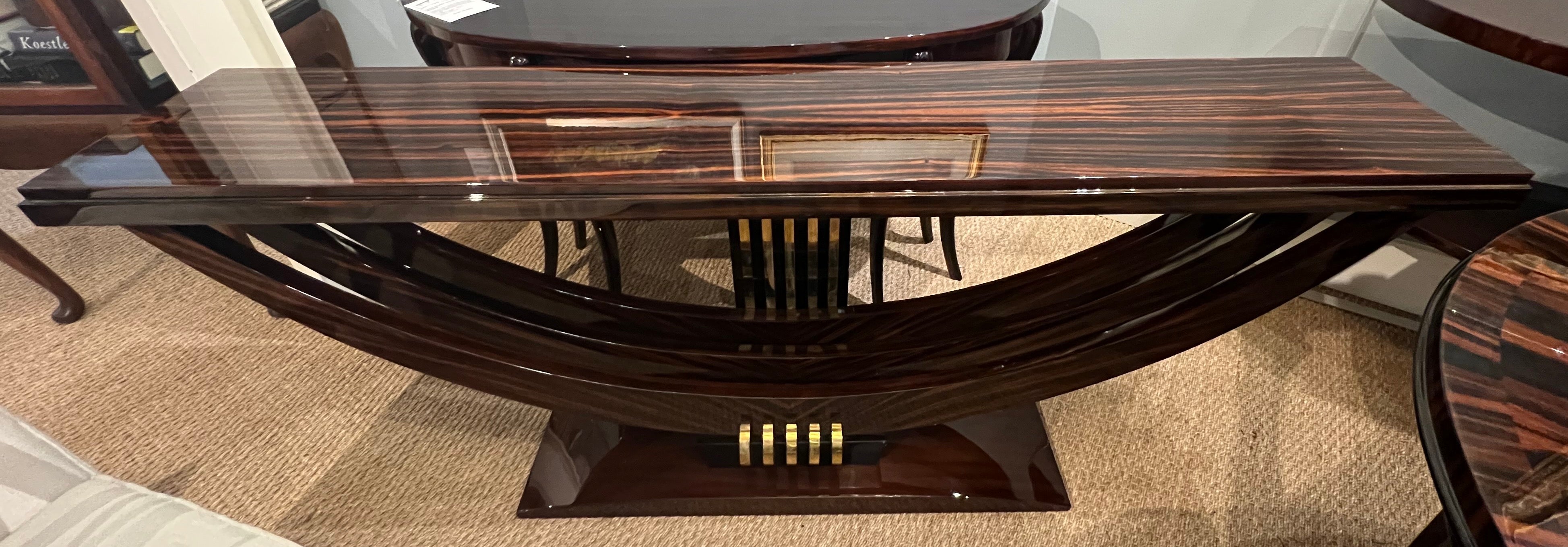 The console is made of Macassar wood. The tabletop is elevated by three curved wooden legs, which are stabilized by a trapezoidal base. On the back of the console, there is a wooden panel with 5 brass decorative lines. 
The condition is very good.