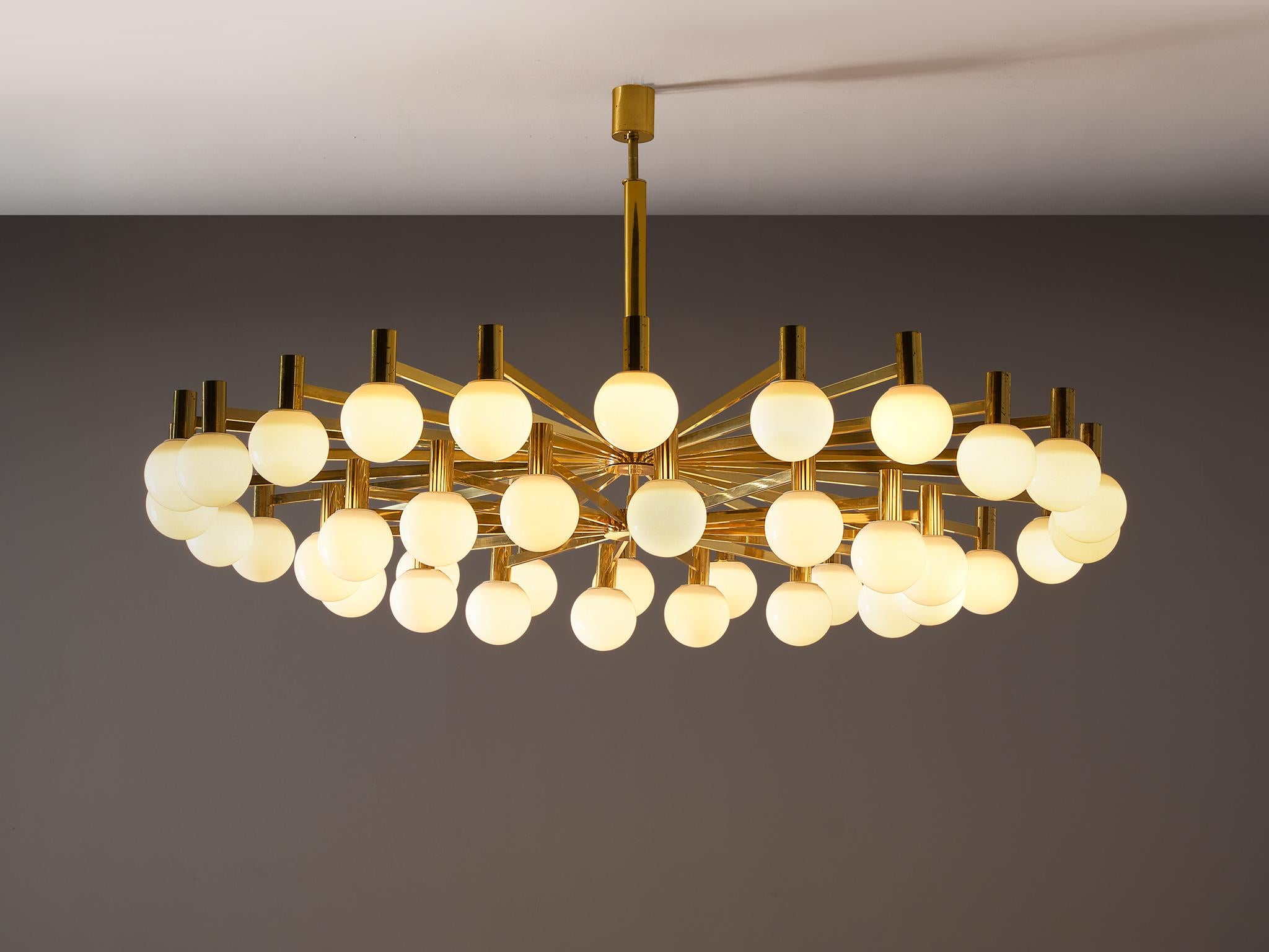 Chandelier, brass, milk glass, Europe, 1970s.

An impressive chandelier of substantial size, this design exemplifies the pinnacle of elegance and sophistication. The chandelier is composed of numerous brass arms that extend outward from a central