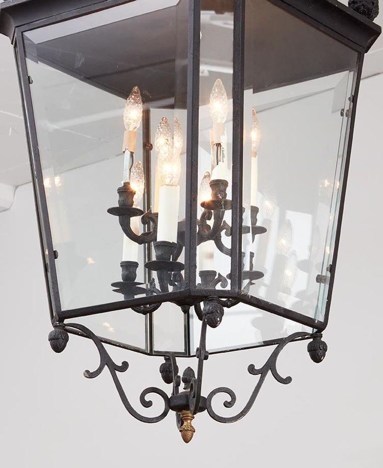 A grand hanging entrance or hall lantern in patinated iron of octagonal form with four large tapering sides and four chamfer corner sides, all with beveled glass, below a domed cornice and above an iron scrollwork base, featuring acorn finials to