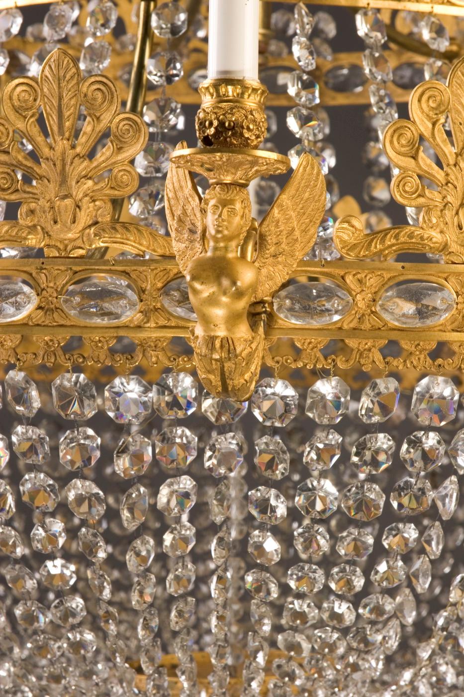 Ce lustre classique de style Empire en bronze d'ore est drapé de cordes de cristaux octogonaux et date du 19e siècle.  Cette pièce antique française offre 18 lumières et une couronne de feuilles d'acanthe réticulées qui arborent de magnifiques