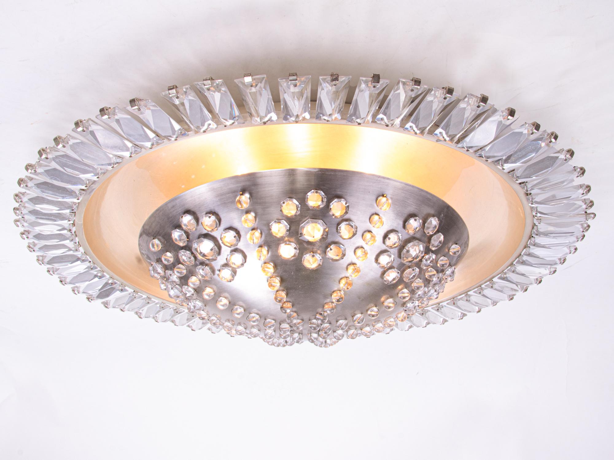 Lustre encastré, grand et élégant, avec un corps central en métal nickelé percé de rosettes de cristaux. Le corps est couronné de prismes de cristal. Le lustre s'illumine magnifiquement et offre beaucoup de lumière. Gemme de l'époque. Avec ce