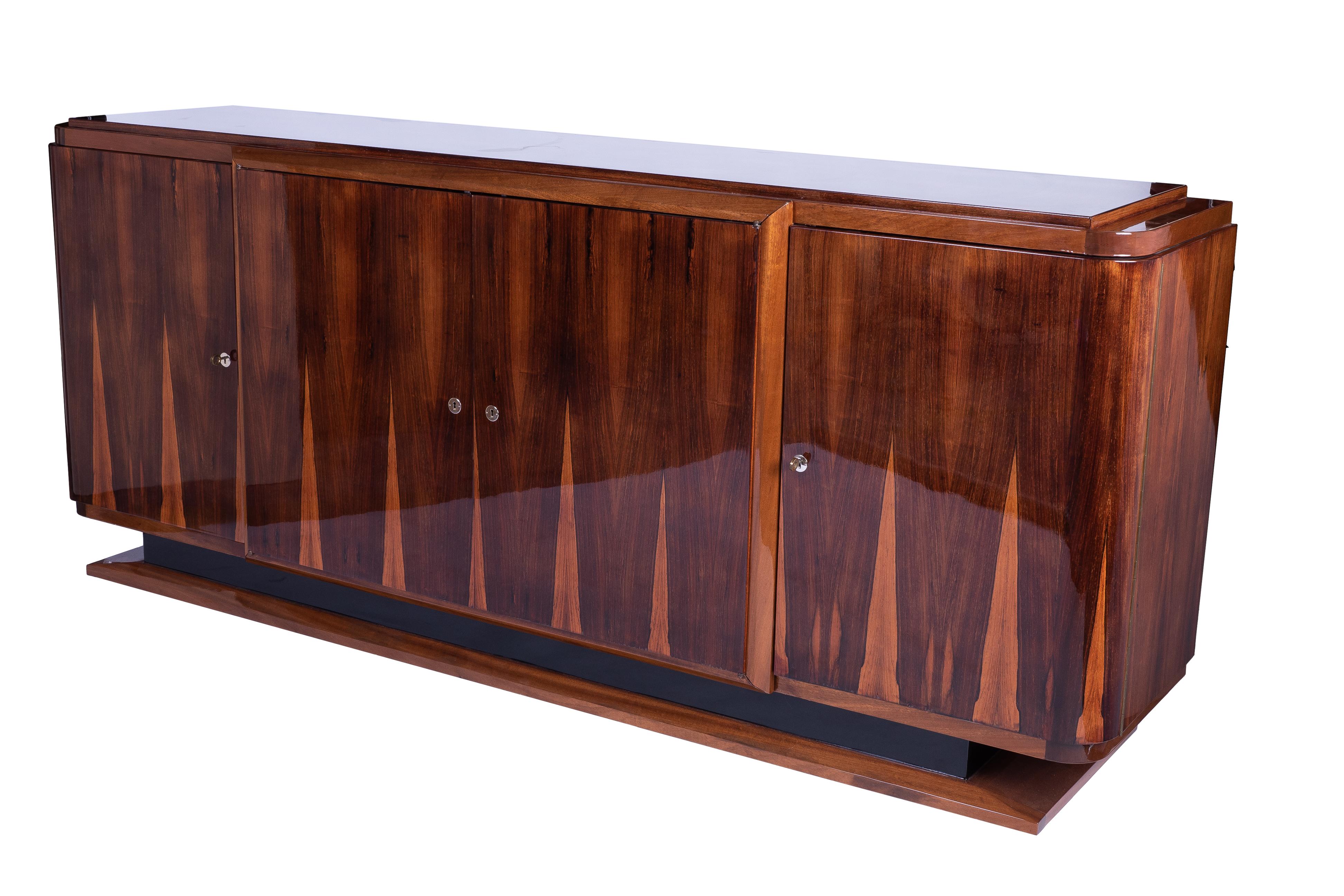 Grand Art Deco sideboard or credenza featuring a solid Mahogany frame veneered in beautifully book matched Rio rosewood and finished in a high gloss lacquer. The piece has large two single doors and one large center double door. Plenty of storage.