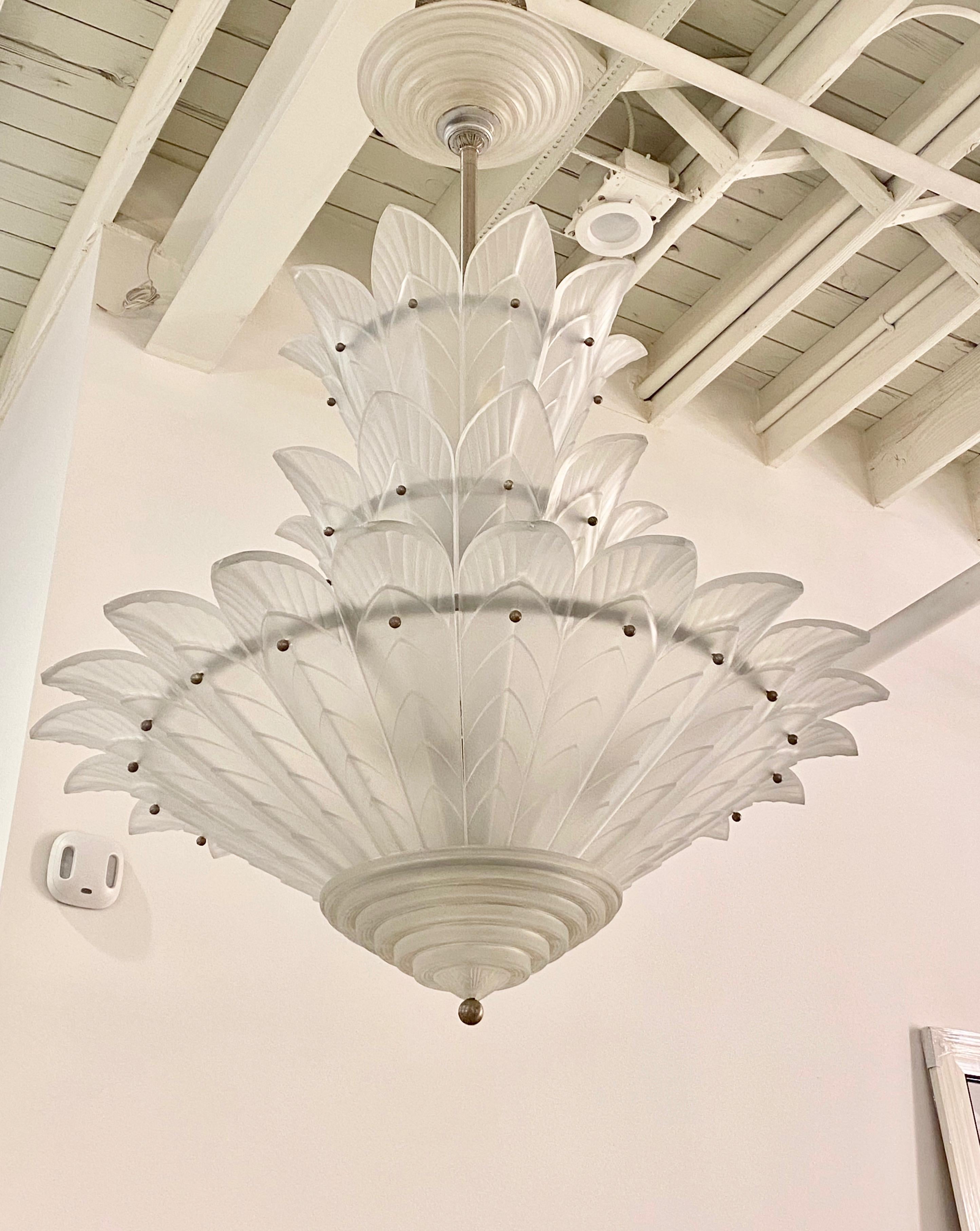 Stunning three tiered French Art Deco chandelier signed by the famous French artist Marius-Ernesto Sabino. Consisting of 38 glass leaf panels in a geometric motif that surround the center glass ribbed bowl with matching glass ceiling plate. The