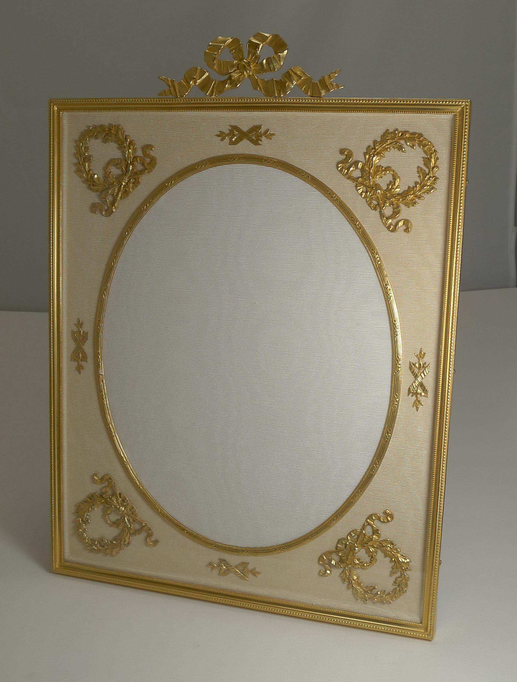An exquisite and very grand French Ormolu picture frame dating to circa 1900. Made from bronze and smothered in gold, the cream silk taffeta below the glass is mounted with a gilded mounts.

The oval aperture measures 9 3/4
