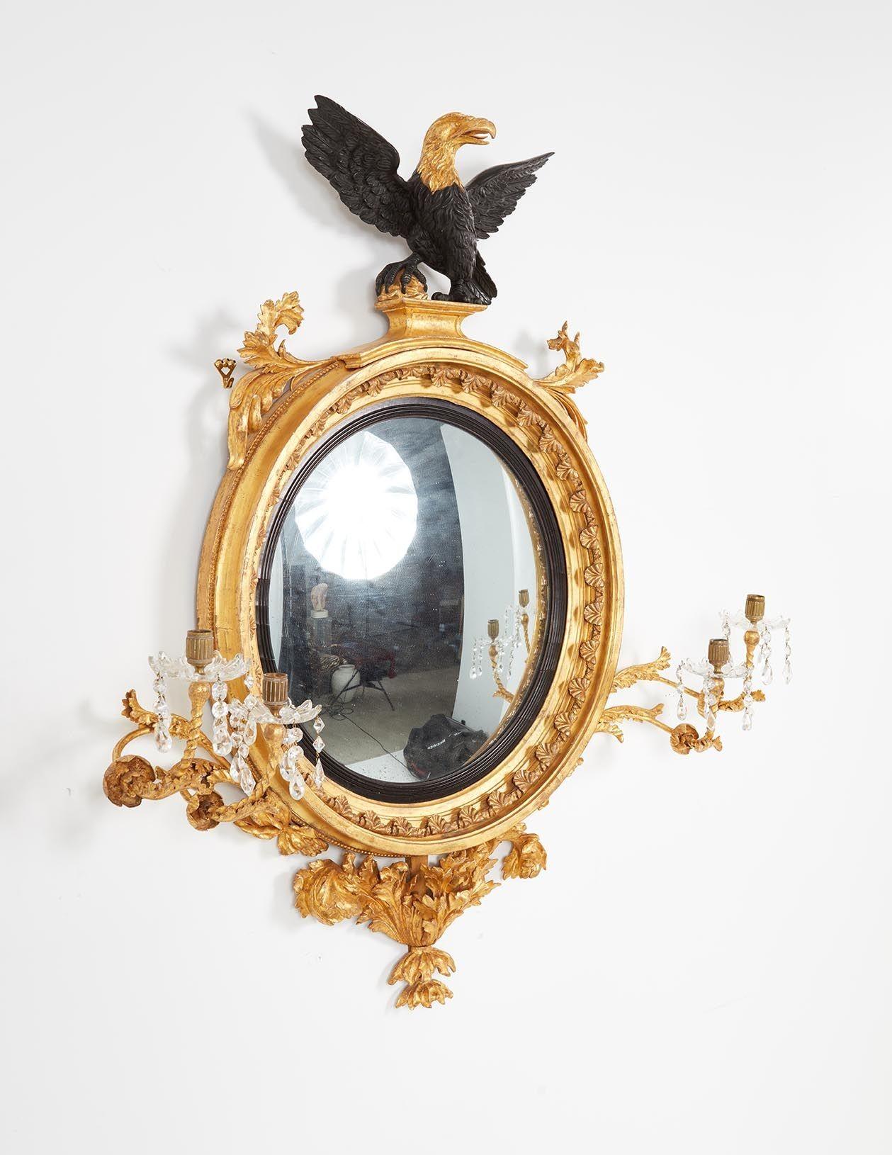 A grand scale and imposing convex gilt mirror with a finely carved two-tone eagle surmount, dramatic gilt leaf shoulders, acanthus leaves around the inside circumference, imposing foliate decorated and rare double girandole arms with crystal drip