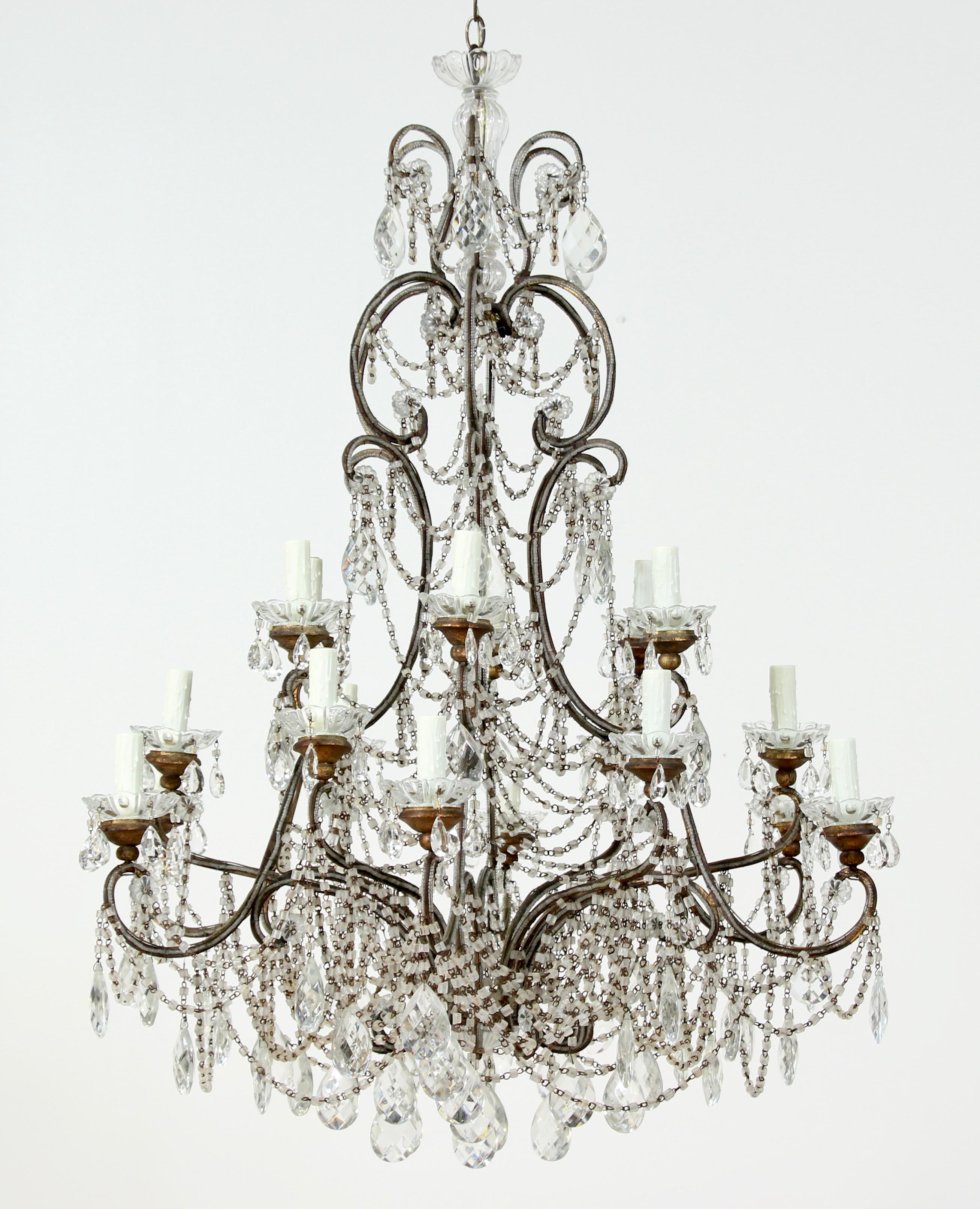 Glorious, 1920s Italian 18-light gilt-iron and crystal beaded chandelier. The chandelier’s gilt-iron frame is all hand beaded and features a beautiful time-worn patina. Each of the chandelier’s 18 glass bobeche rest on giltwood mounts. A generous