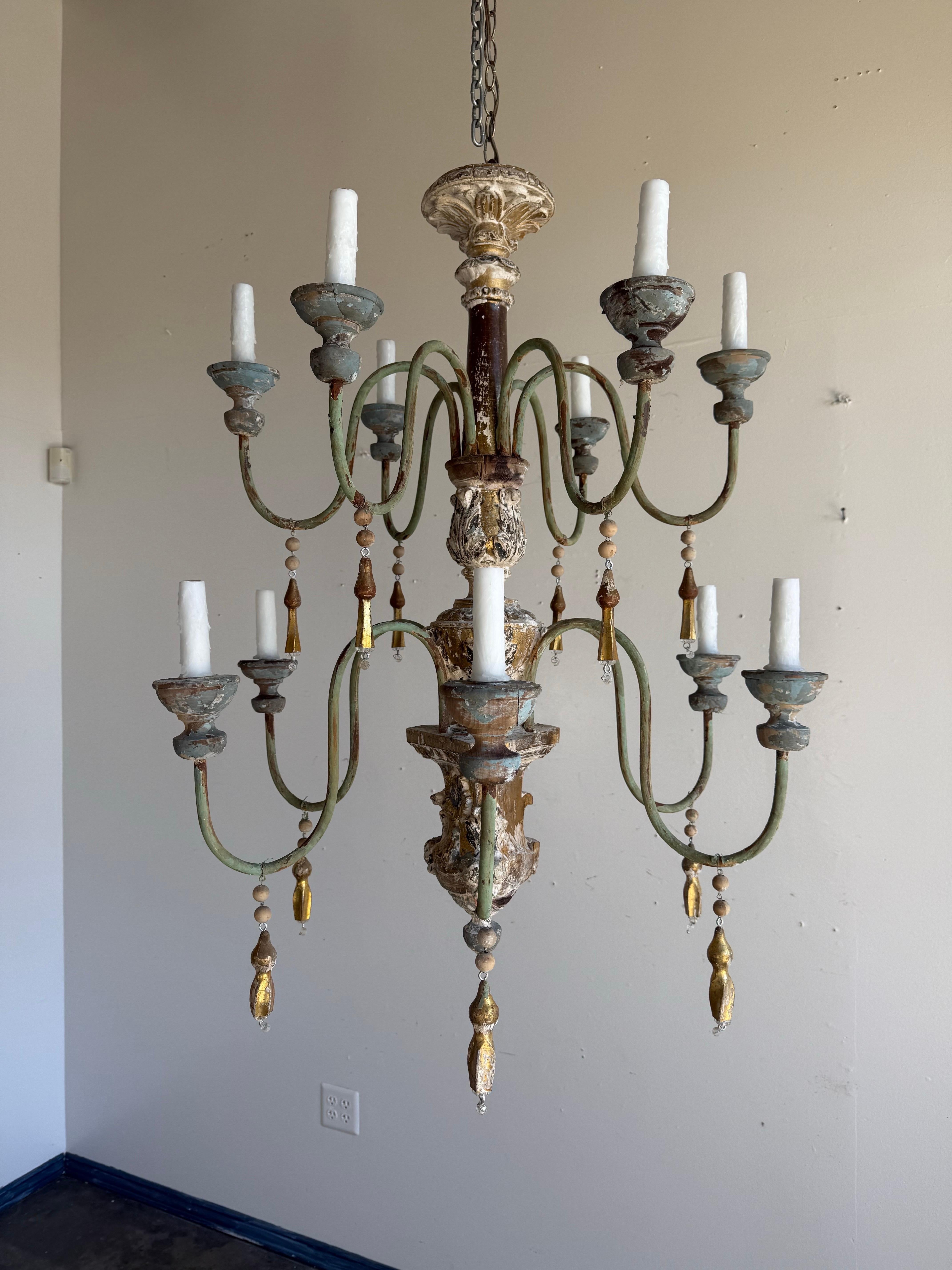 A spectacular Italian painted and giltwood chandelier, early 20th century, in the Baroque and Rococo revival taste. This large twelve-light fixture features a carved and turned central column with traces of original polychrome paint and parcel